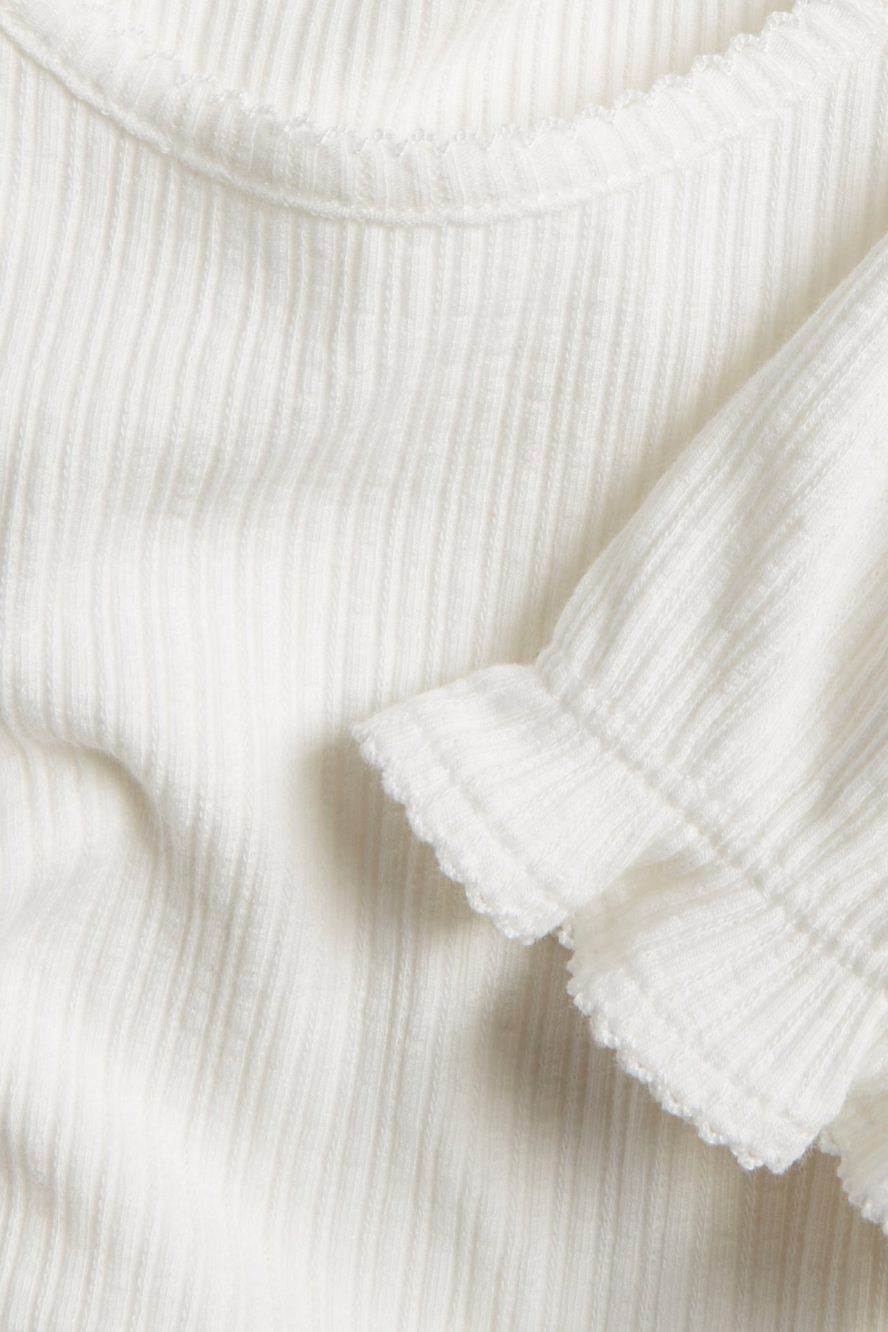Nahaufnahme eines cremefarbenen gerippten Jersey-Tops mit kurzen Puffärmeln und Picot-Besatz.