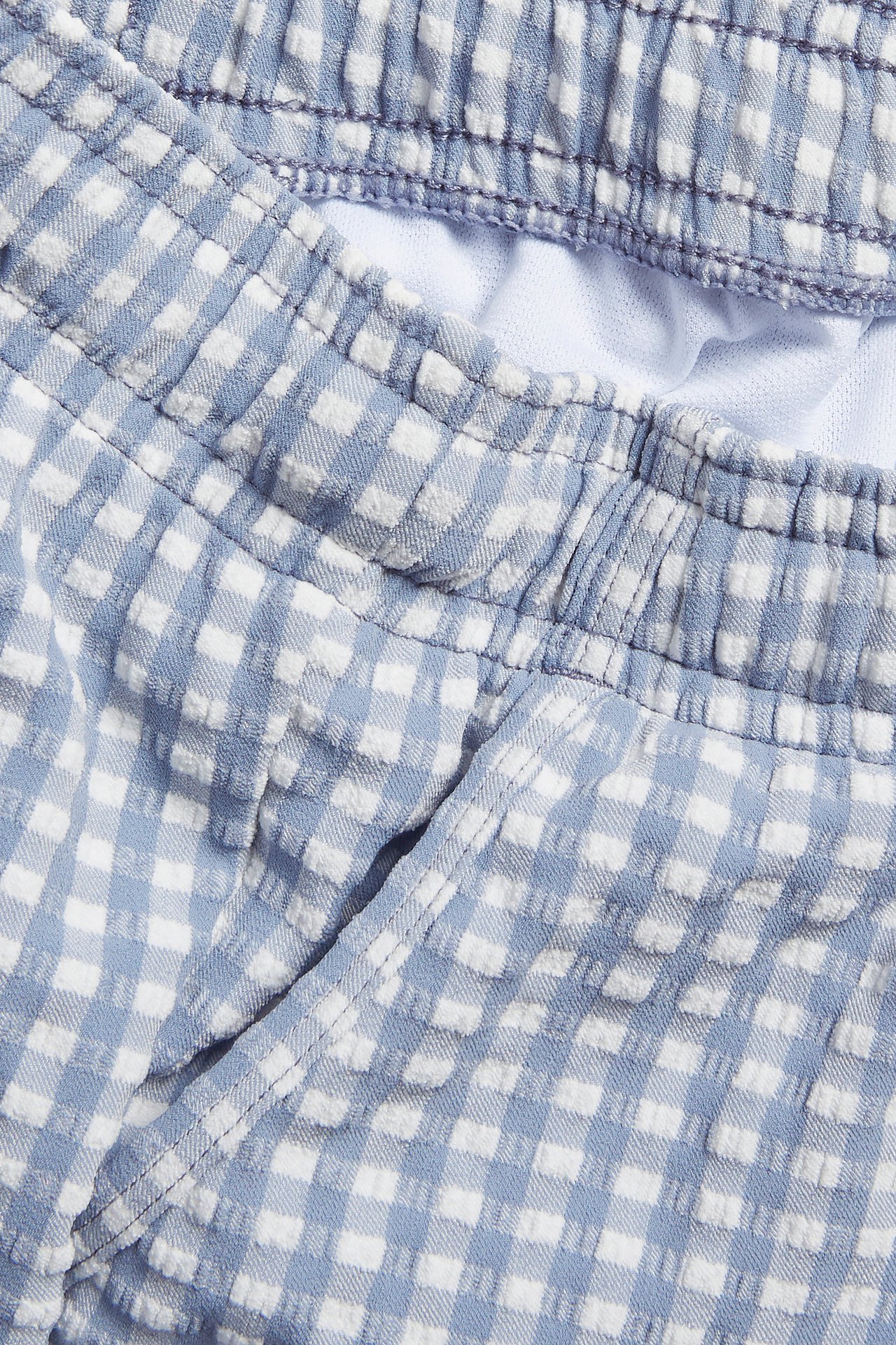 Nahaufnahme von blau-weiß karierten Seersucker-Badeshorts mit elastischem Bund und Taschen.