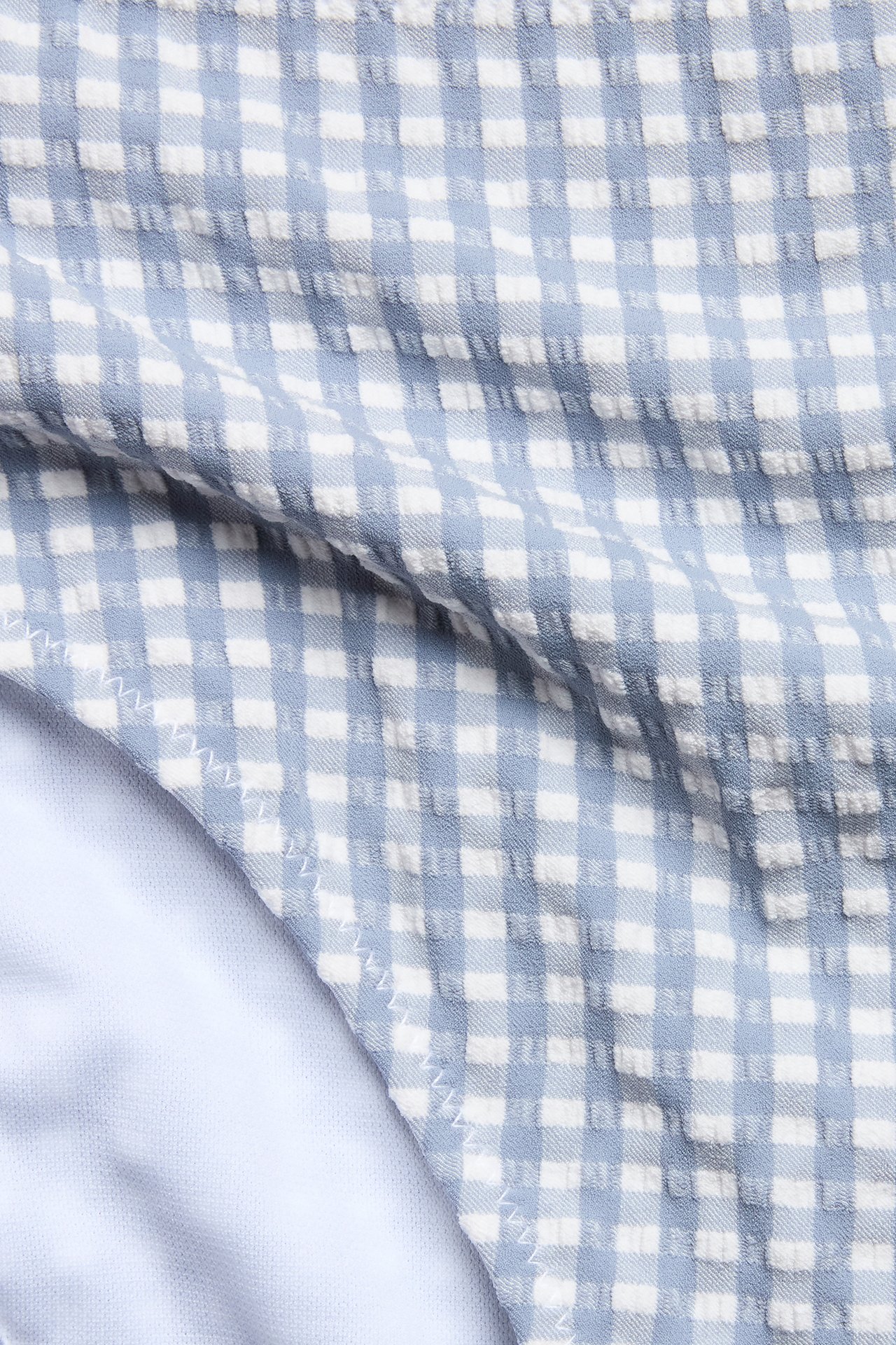 Close-up of a woman's high-waisted blue and white checked bikini bottom with textured fabric and white lining.