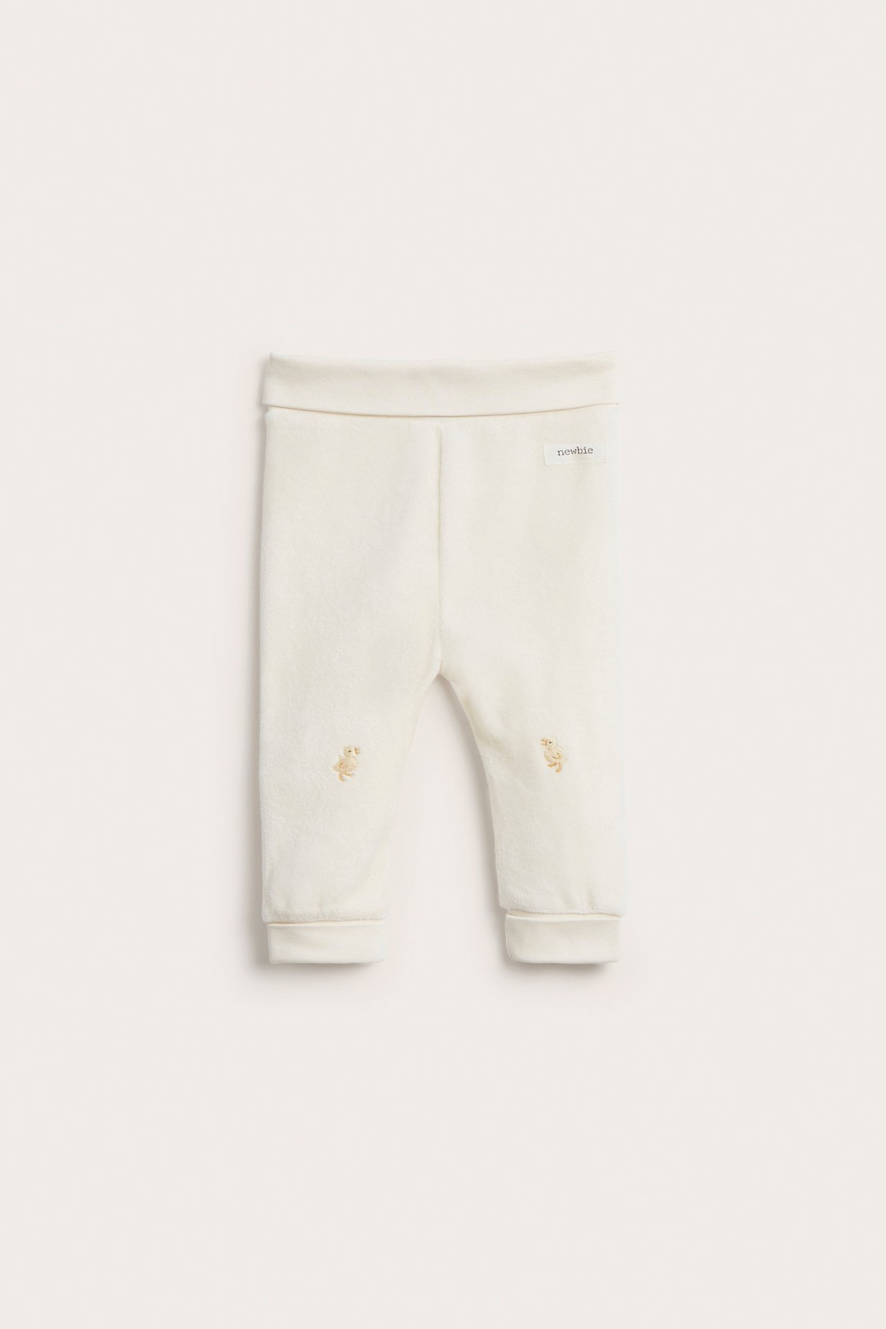 Front view of off-white velour baby leggings with a foldable waist and knee embroidery.