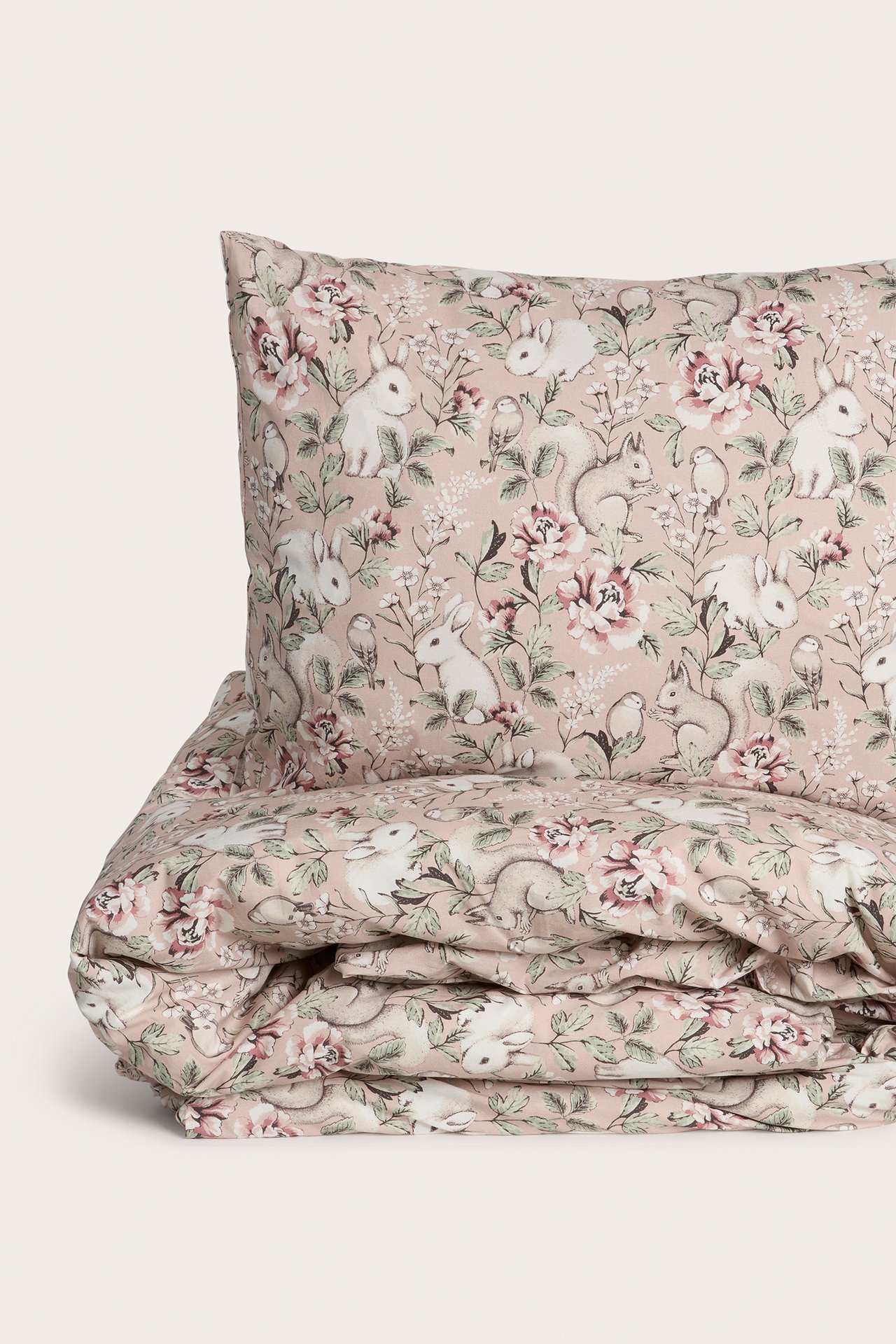 Nahaufnahme eines rosa Baumwoll-Bettwäschesets mit detailliertem Tier- und Blumenmuster.