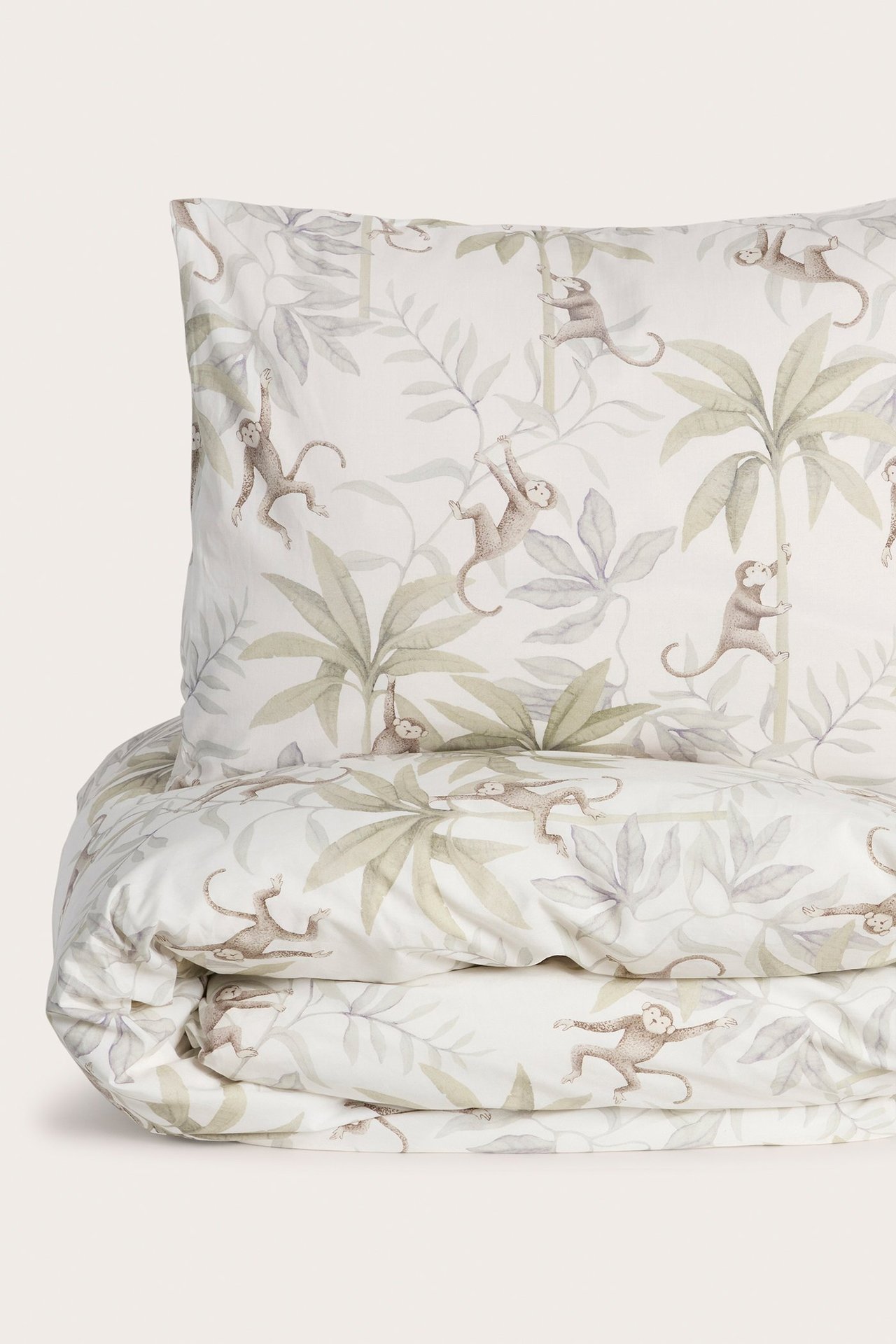 Vorderansicht eines cremefarbenen Baumwoll-Bettwäschesets mit Dschungelmuster aus Affen und Palmenblättern.