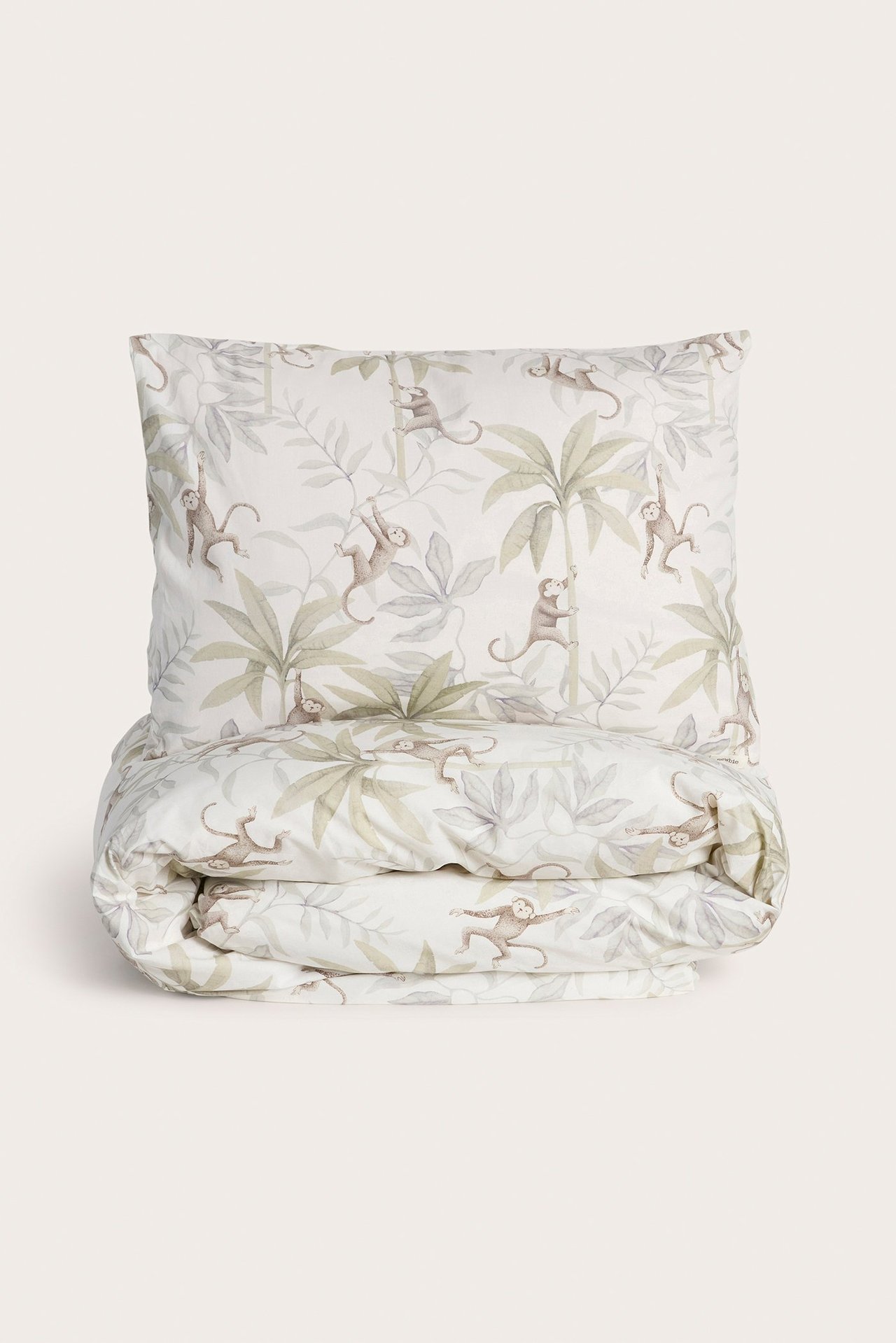 Vorderansicht eines cremefarbenen Baumwoll-Bettwäschesets mit Dschungelmuster aus Affen und Palmenblättern.