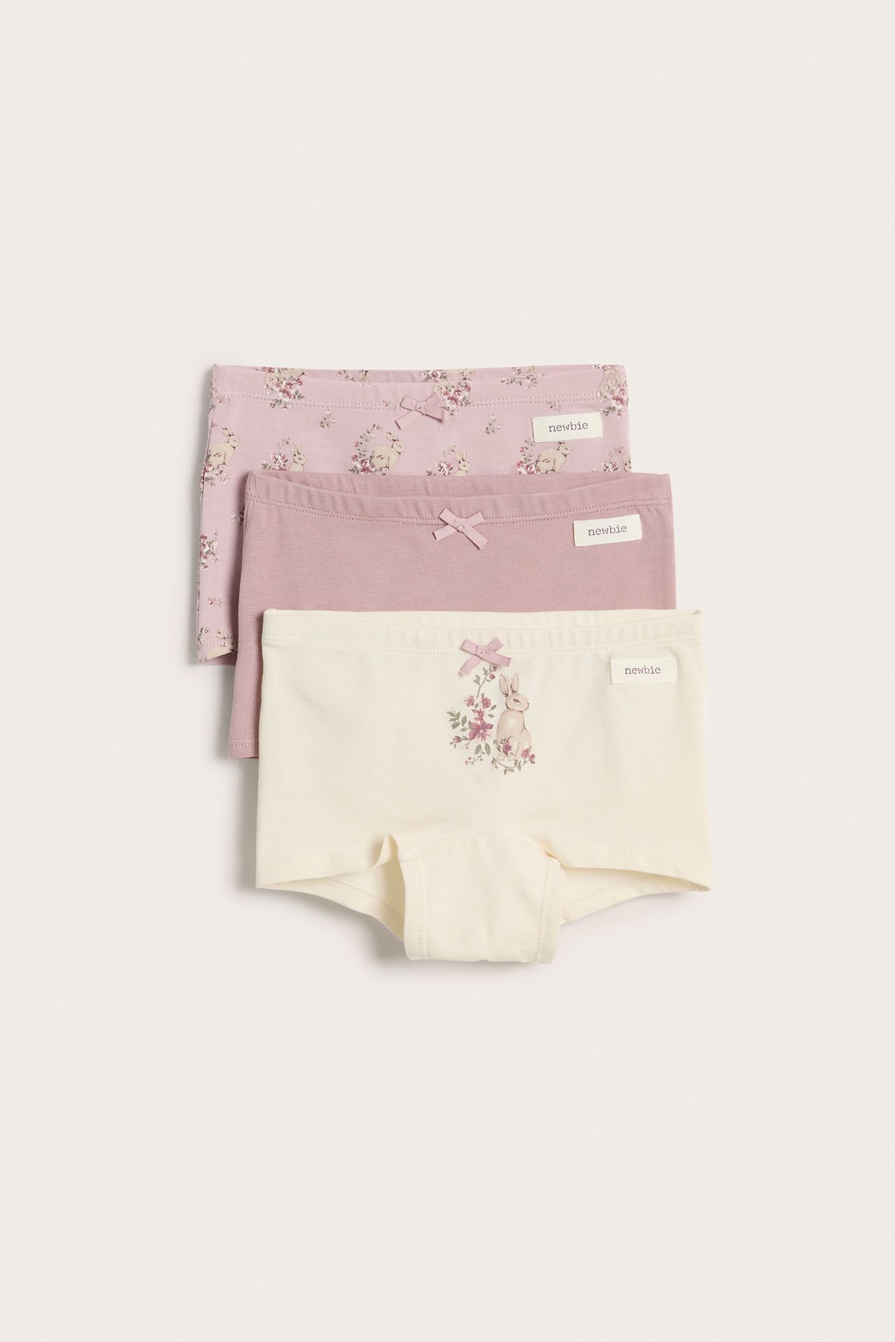 Vorderansicht von drei Kinder-Baumwollboxershorts mit Schleifen: cremeweißer Hase, einfarbig helllila, rosa Blumen.