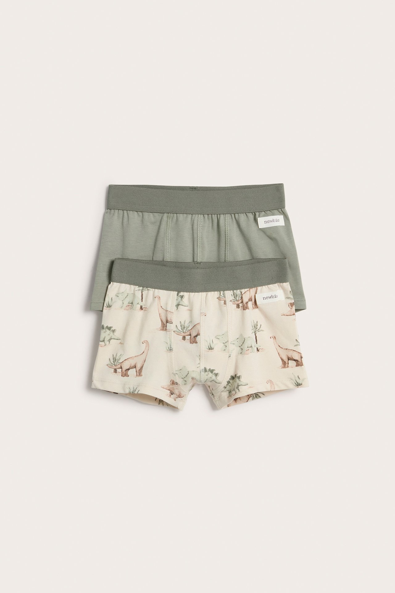 Vorderansicht: Kinder-Boxershorts in Hellbeige mit Dinosaurier-Print und grünem Bund, sowie einfarbige grüne.