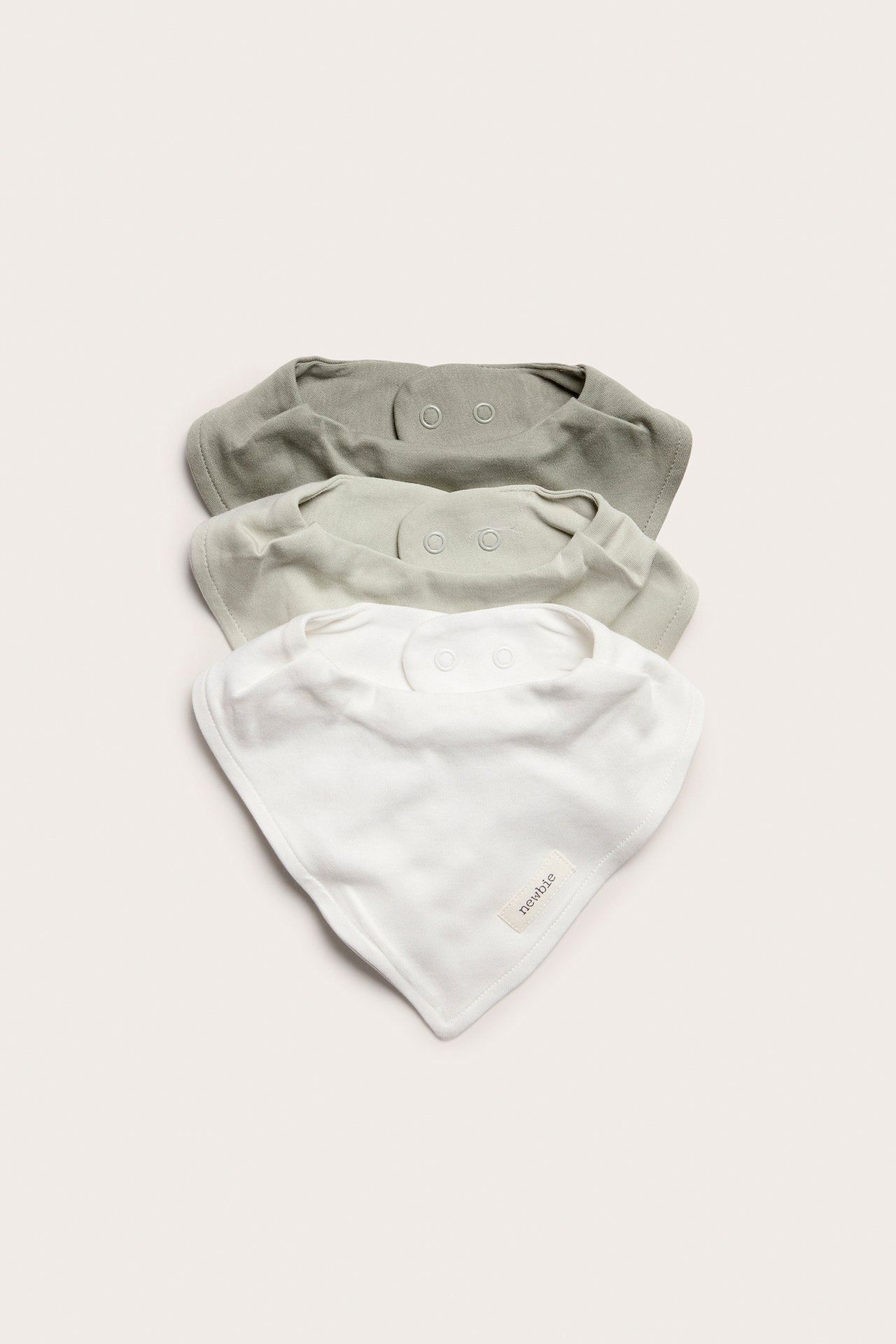 Top-down view of three baby bandana bibs in white, light grey-green, and dark grey-green soft cotton with snap buttons.