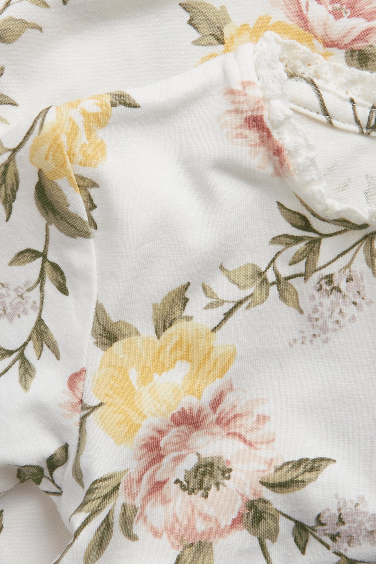 Close-up of an off-white baby long-sleeved jersey bodysuit with a floral pattern and lace trim.