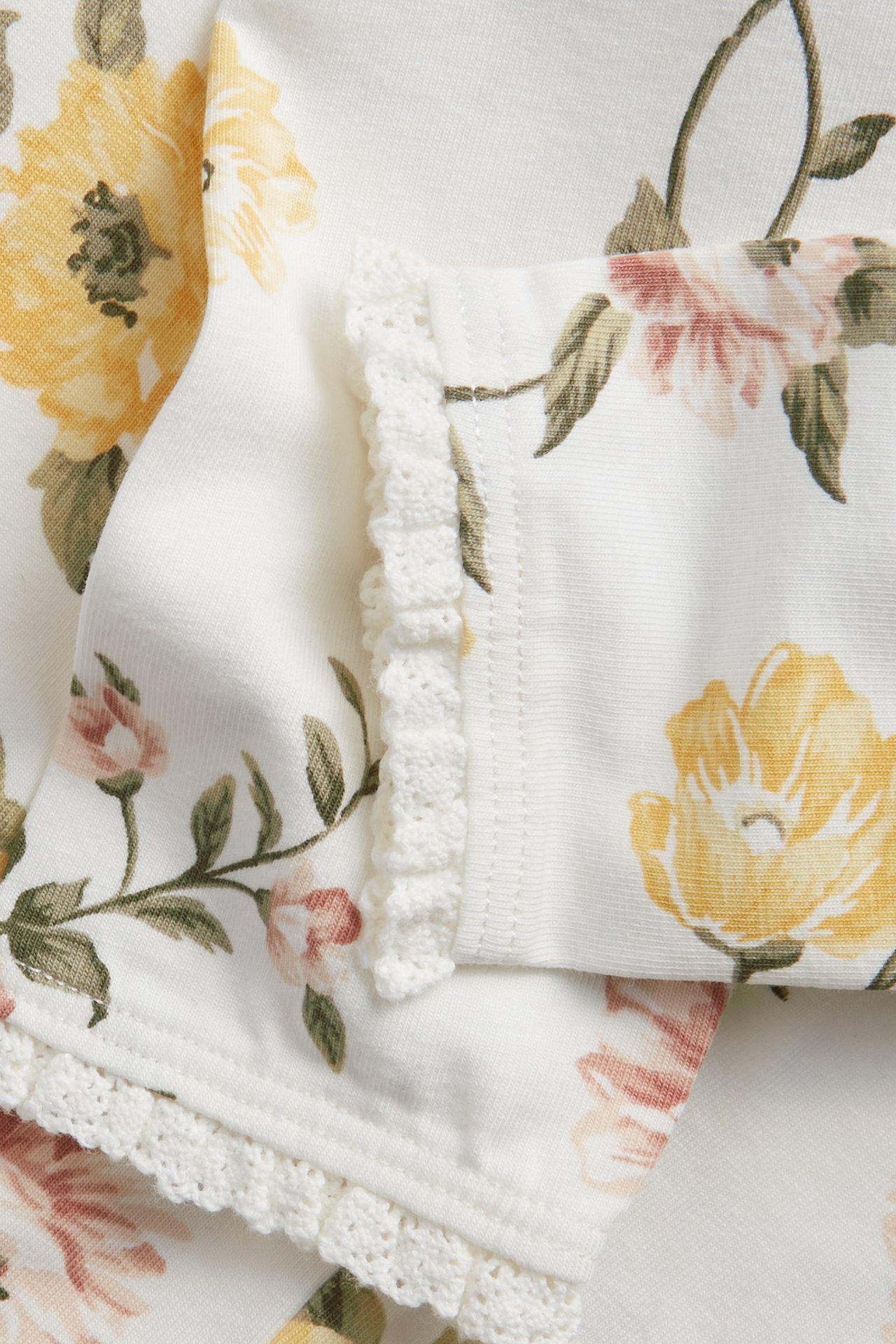 Close-up of off-white floral leggings with yellow and pink flowers and crocheted lace trim.