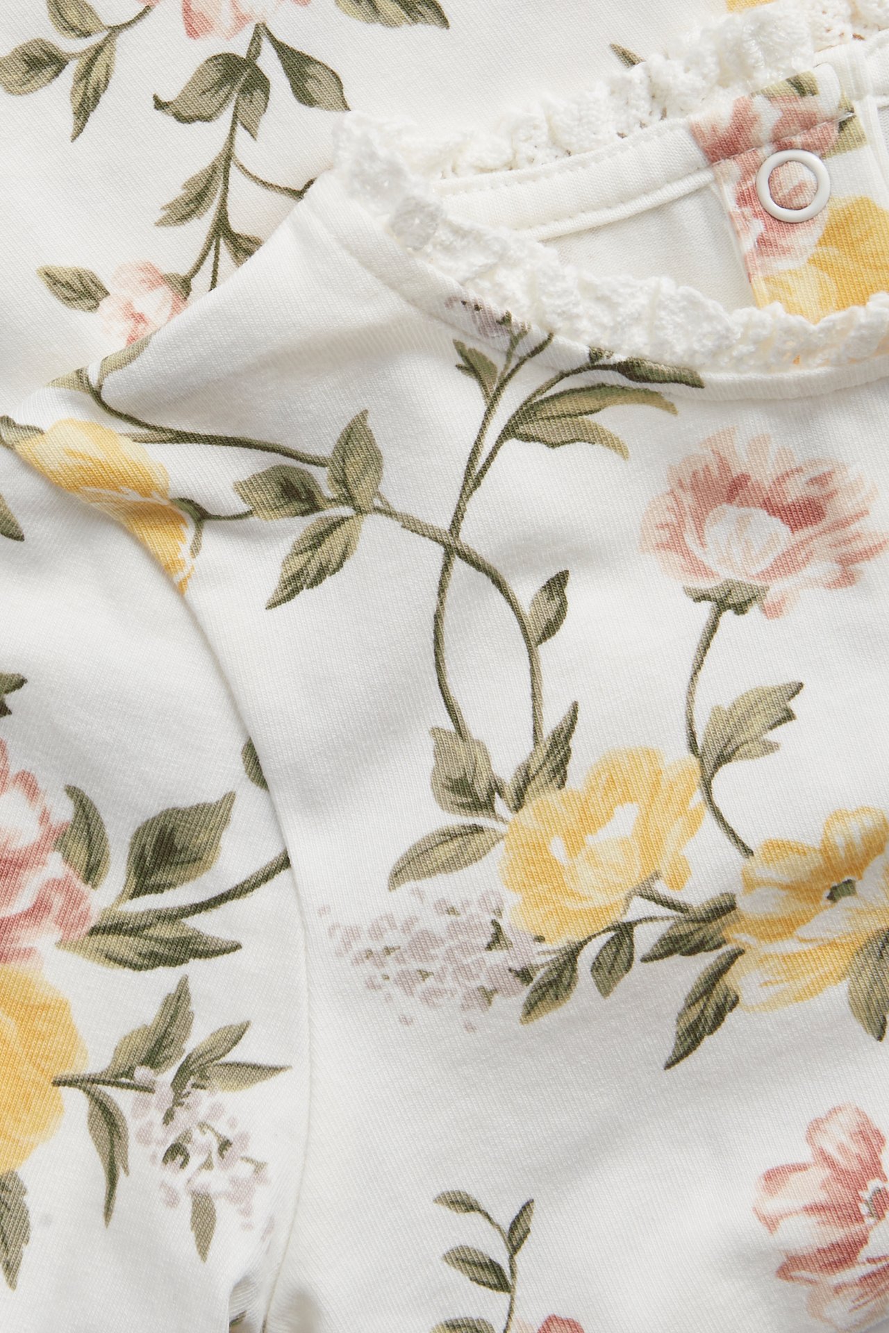 Close-up of an off-white baby/kid's floral jersey top with yellow and pink roses and a lace-trimmed neckline.