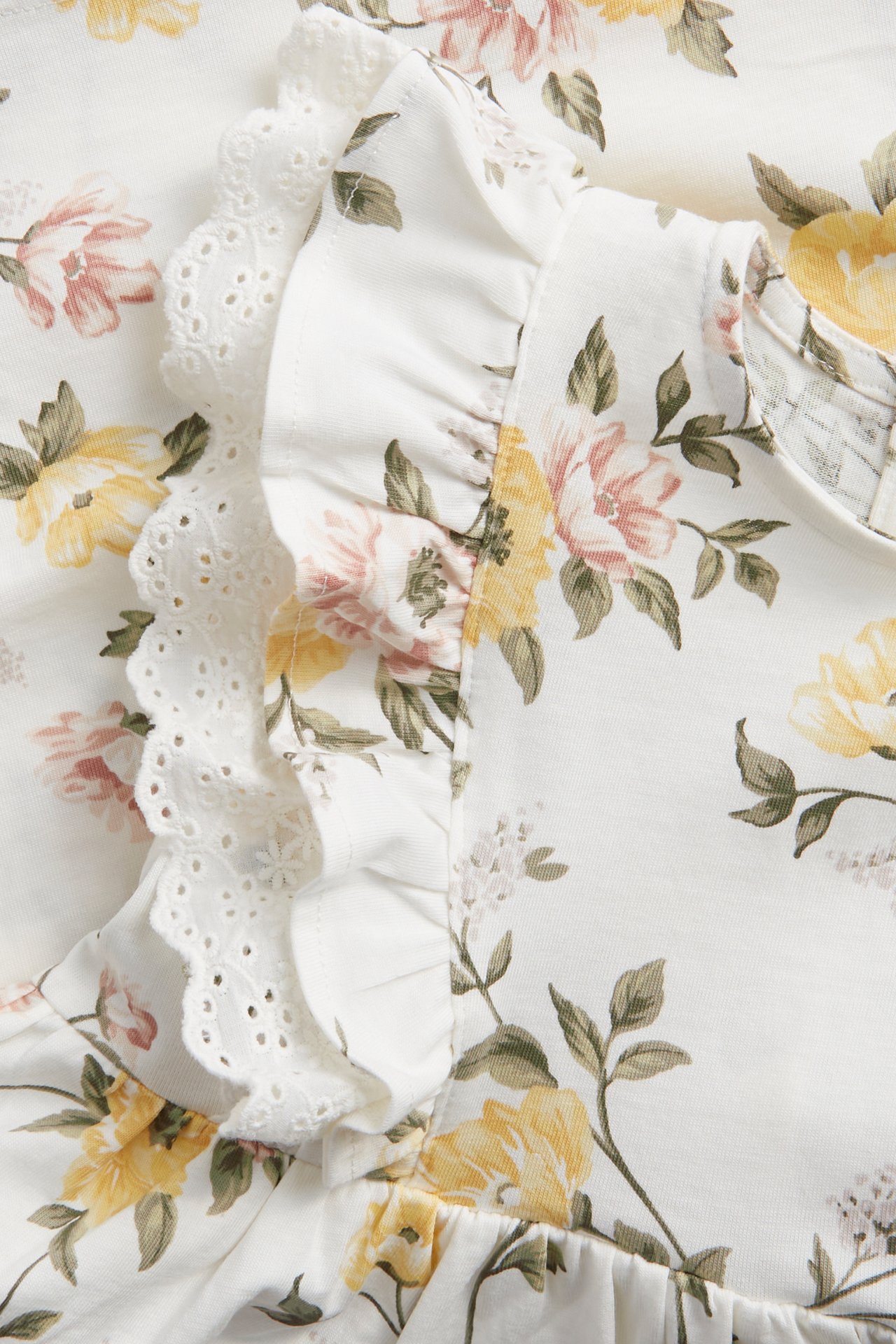 Nahaufnahme eines cremefarbenen Baumwoll-Jerseykleides mit gelbem und rosa Blumenmuster und Rüschenspitzenbesatz.
