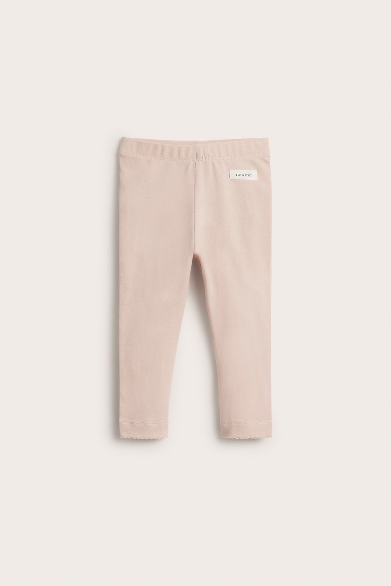 Front view of light pink baby leggings with an elastic waist and scalloped lace trim at the hem.