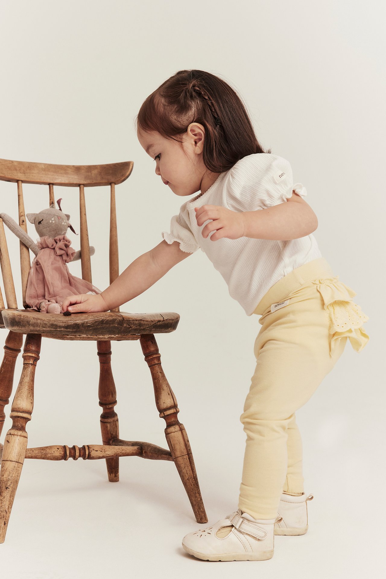 Seitenansicht eines Baby-Mädchens in gelben Leggings mit Rüschen, weißem Ripp-Top und hellbeigen Schuhen.