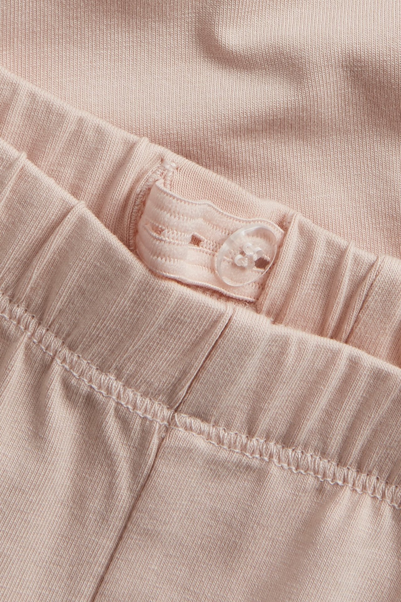 Close-up of light pink baby leggings, showing an adjustable elastic waistband with a clear button.
