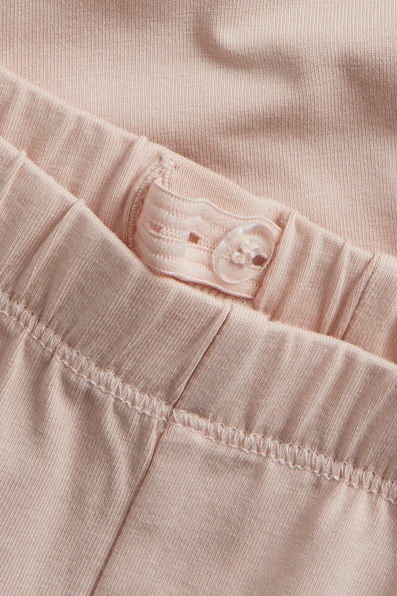 Close-up of light pink leggings with an adjustable elastic waistband and a transparent button.