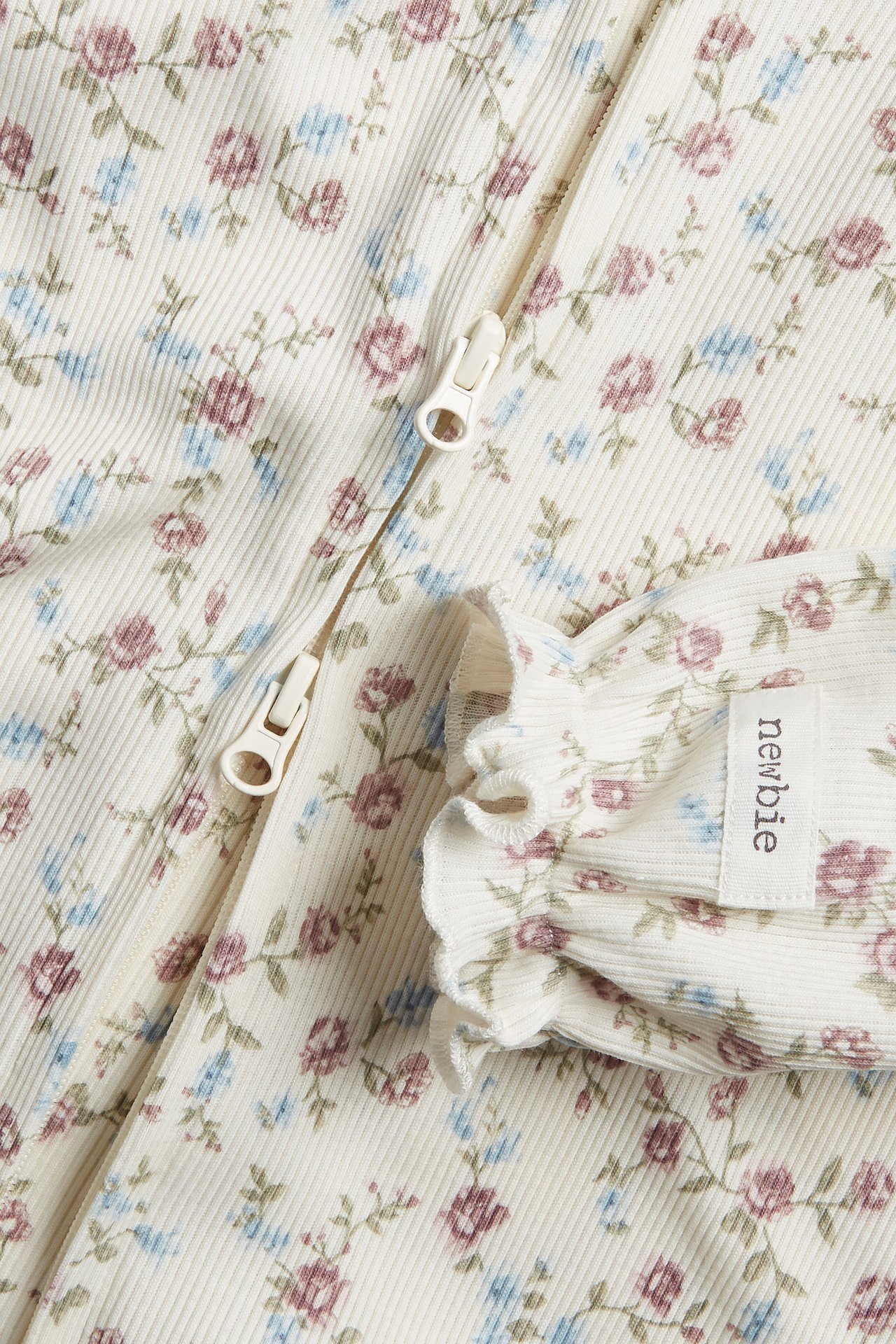 Close-up of an off-white ribbed baby pyjamas with a floral print, two-way zipper, and ruffled cuffs.