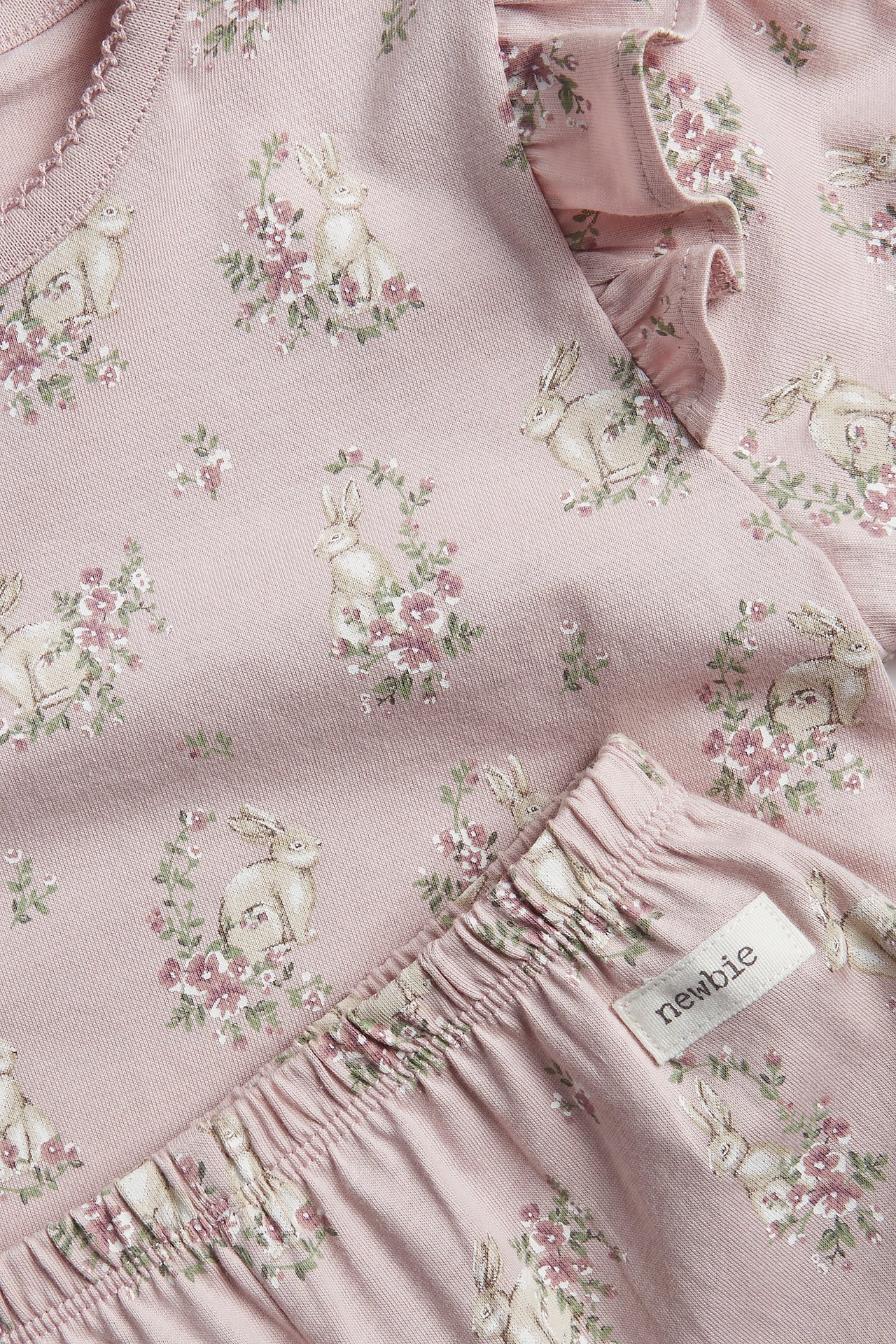 Close-up of kid's pink cotton pyjamas with floral rabbit print, shoulder ruffles, elasticated waist.