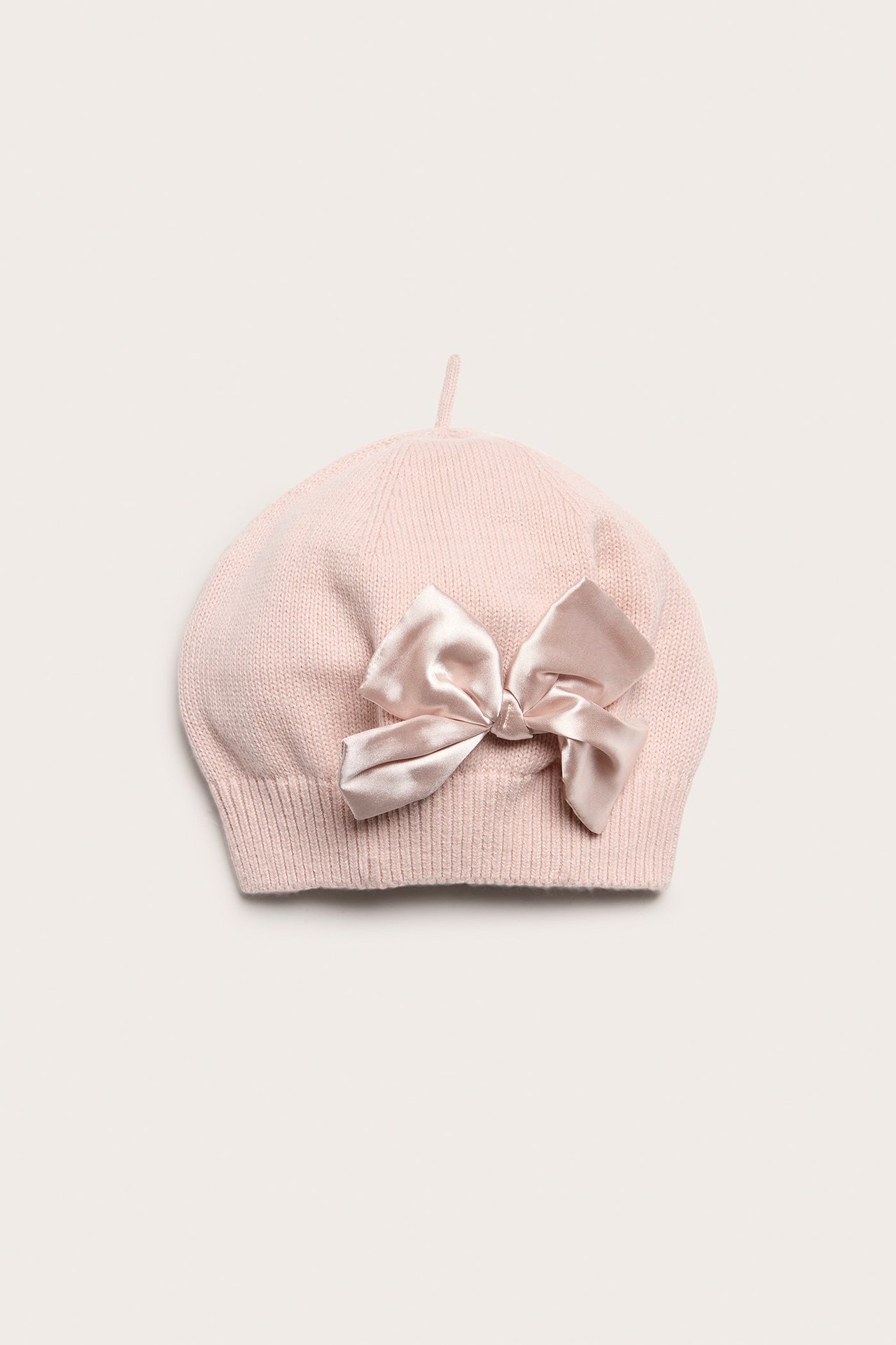 Front view of a light pink knitted beret with a shiny, woven light pink bow.