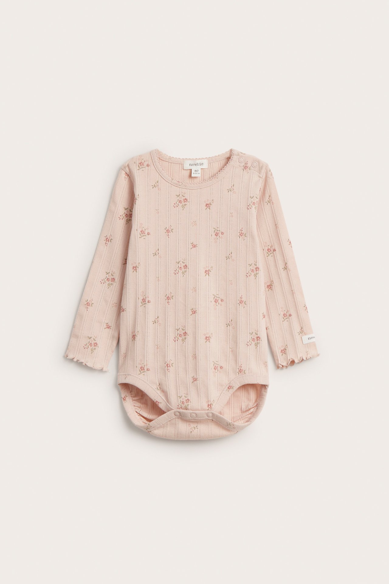 Vorderansicht: hellrosa Baby Langarm-Pointelle-Rippbody mit Blumenmuster, Wellenkanten, Druckknöpfen.
