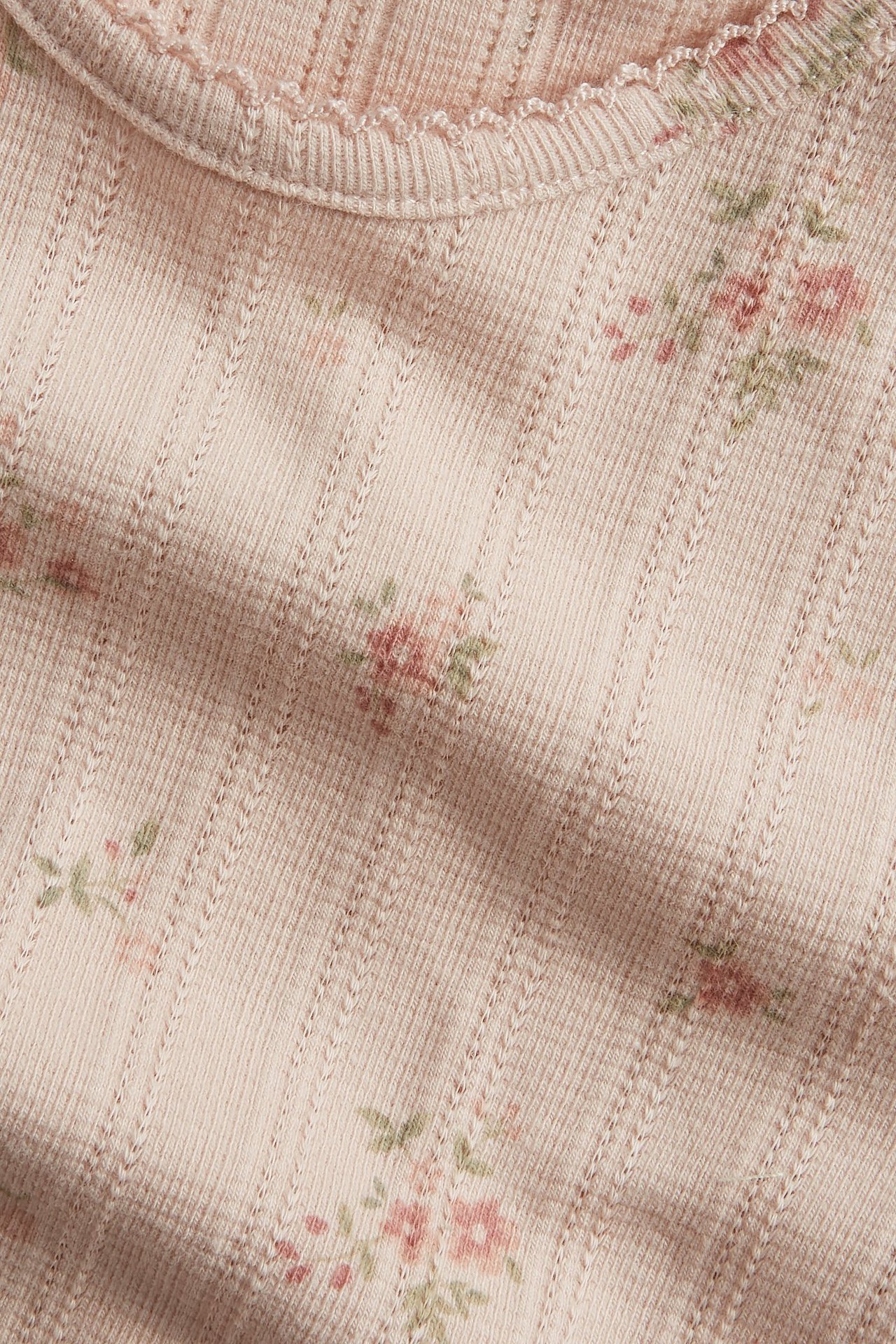 Close-up of a light pink pointelle rib long-sleeved top with a floral pattern and wavy neckline.