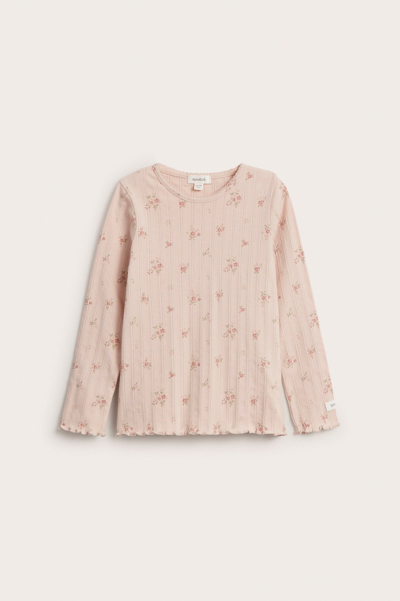 Front view of a light pink kid's long-sleeved pointelle rib top with small floral print and wavy edges.