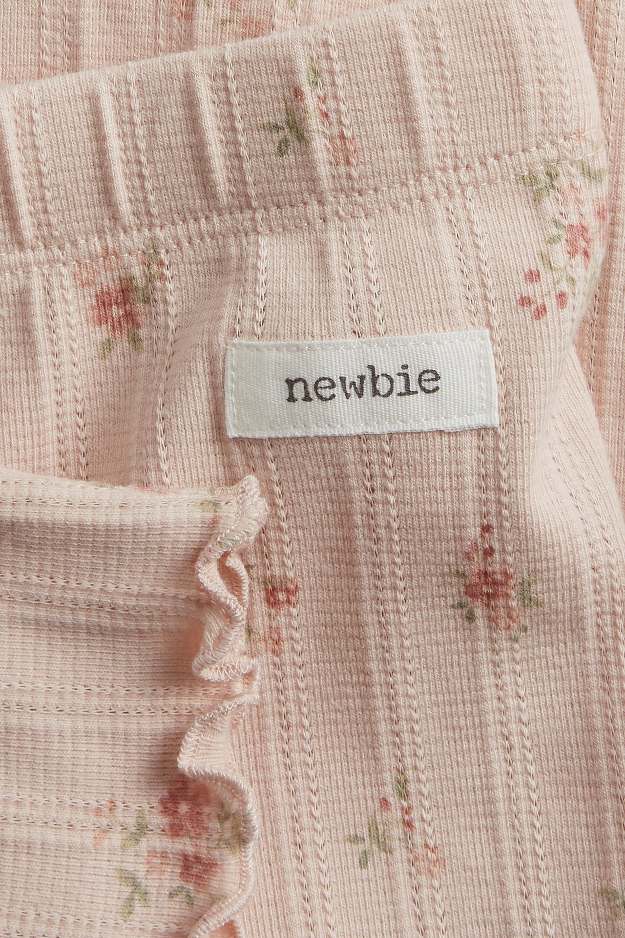 Close-up of light pink pointelle rib leggings with a floral print, wavy edge, and a 'newbie' label.