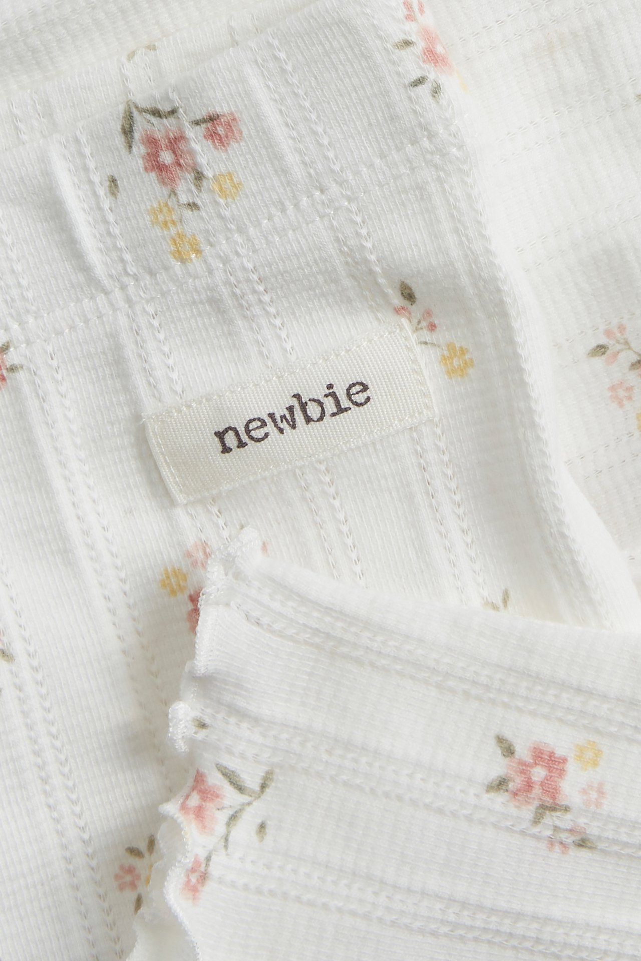 Close-up of offwhite pointelle rib leggings with floral print, wavy edge, and a 'newbie' label.