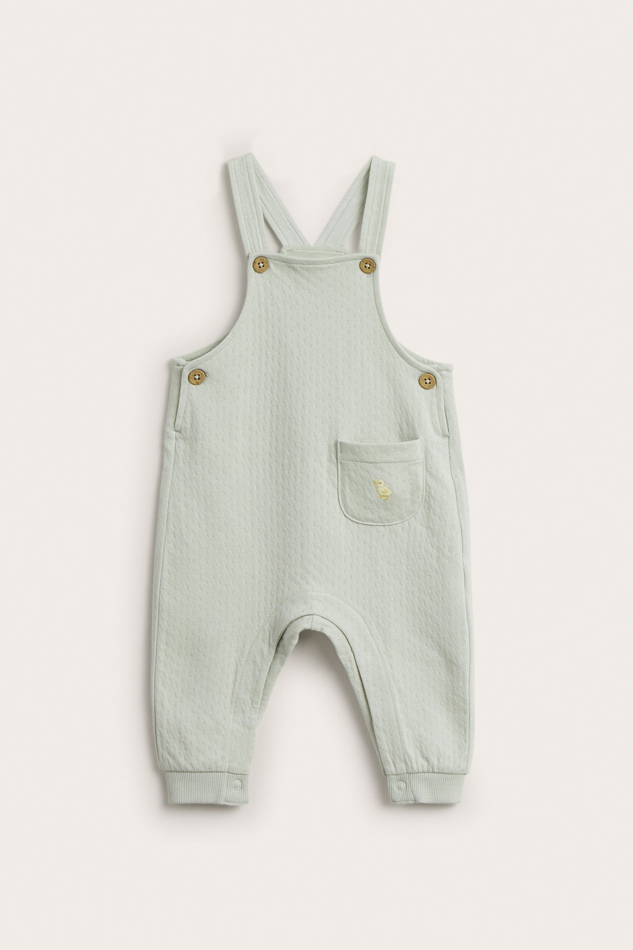 Vorderansicht hellgrüner Baby-Baumwoll-Latzhose mit gesteppter Textur, verstellbaren Trägern und bestickter Tasche.