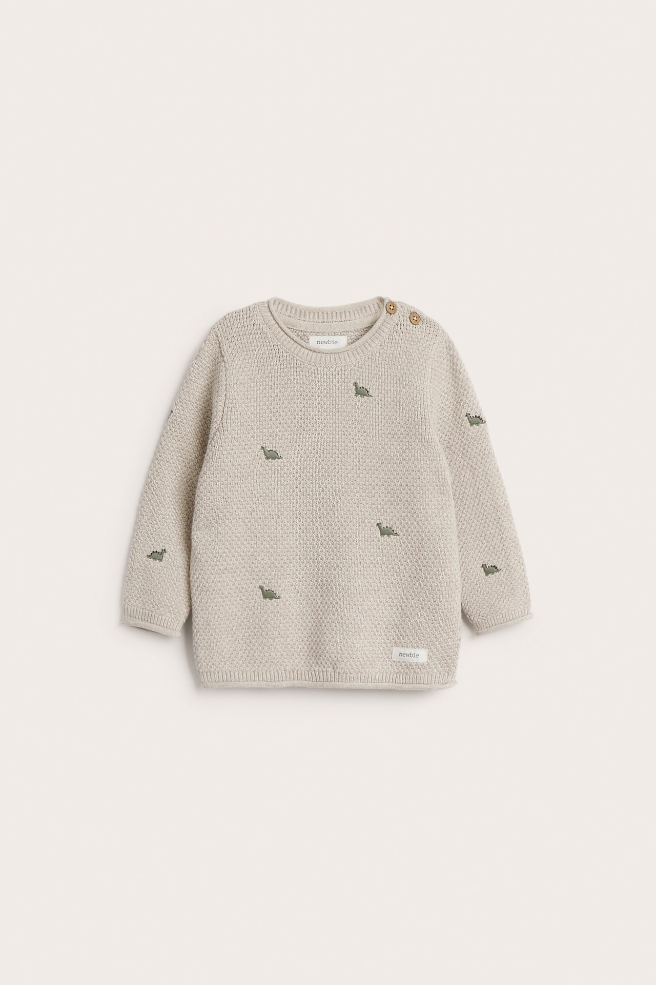 Front view of a beige knitted baby sweater with green dinosaur embroidery and shoulder buttons.