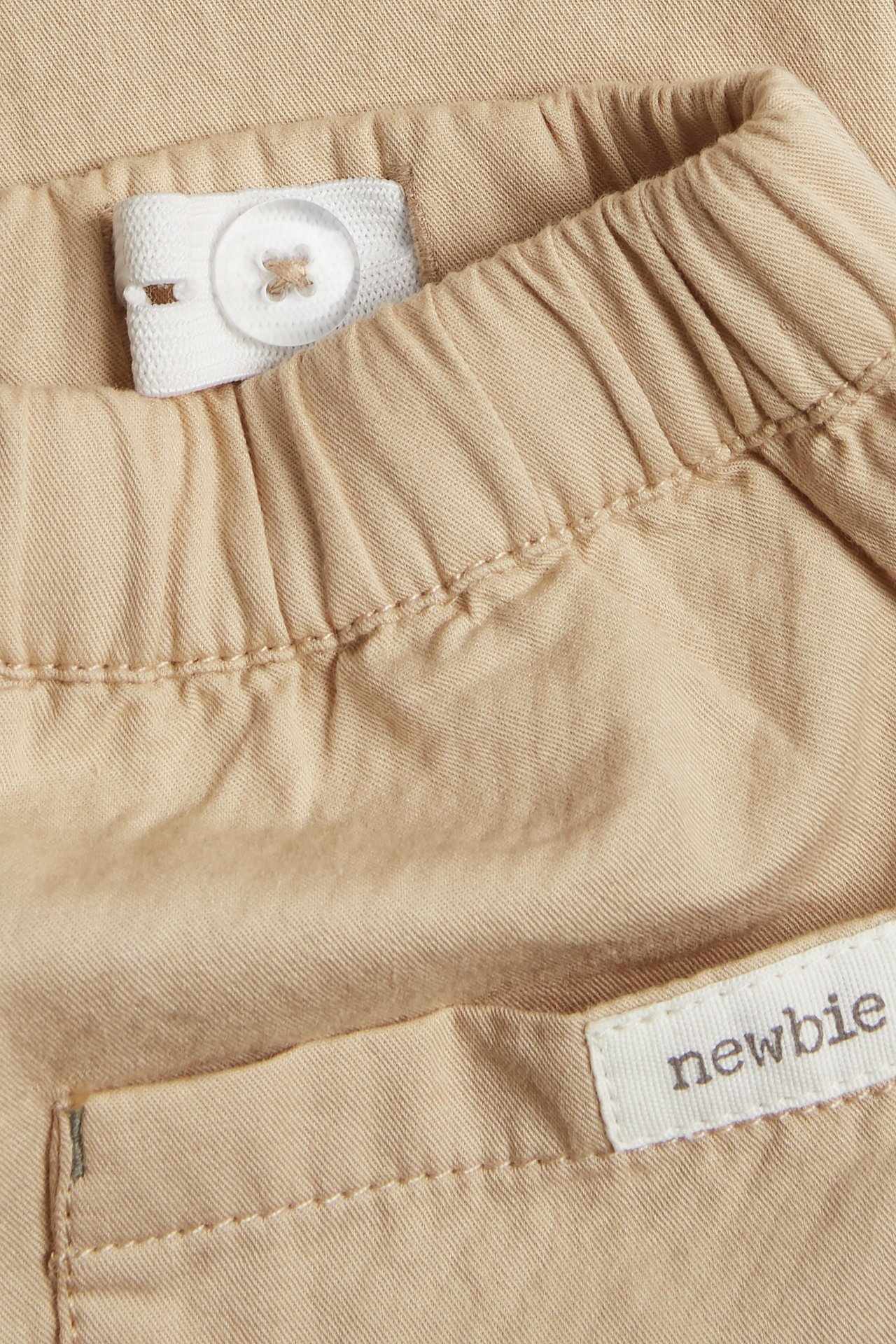 Nahaufnahme beiger gewebter Baumwollhose mit elastischem Bund und verstellbarem Knopf.