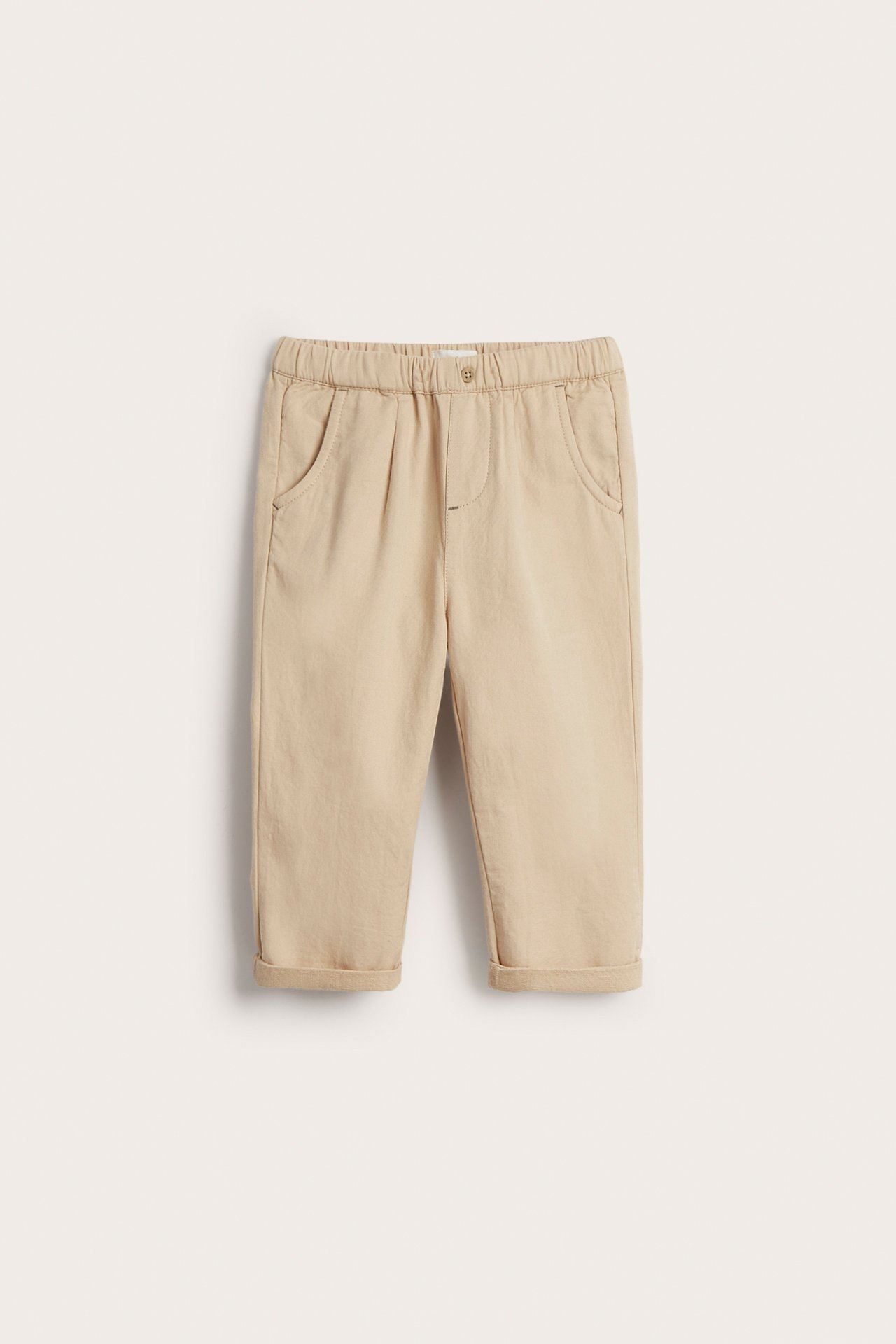 Vorderansicht: Beige gewebte Baumwollhose für Kinder mit Gummizug, Vordertaschen und umgekrempelten Bündchen.