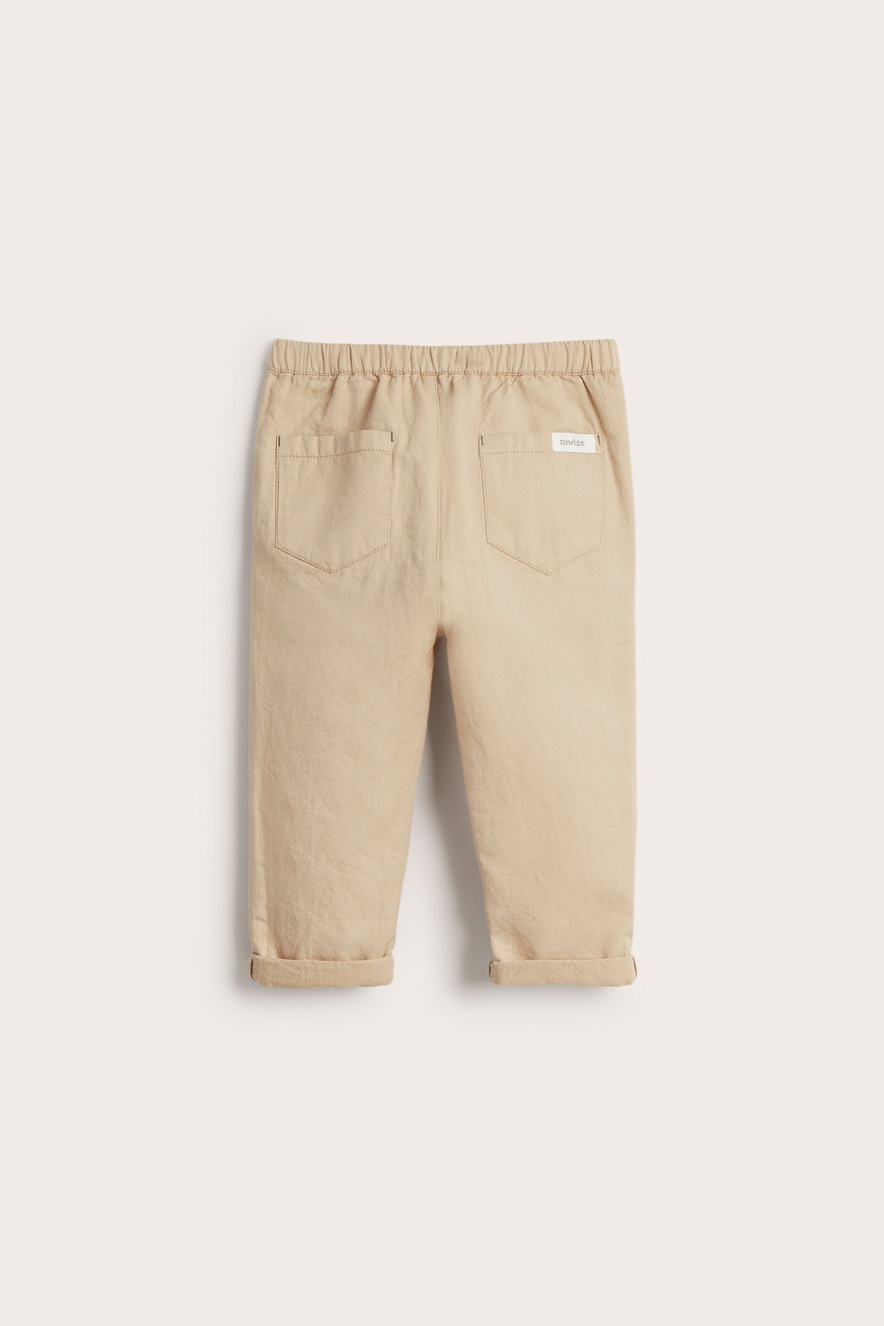 Rückansicht beiger gewebter Baumwollhose für Kinder mit Gummizugbund, zwei Gesäßtaschen und umgekrempelten Säumen.