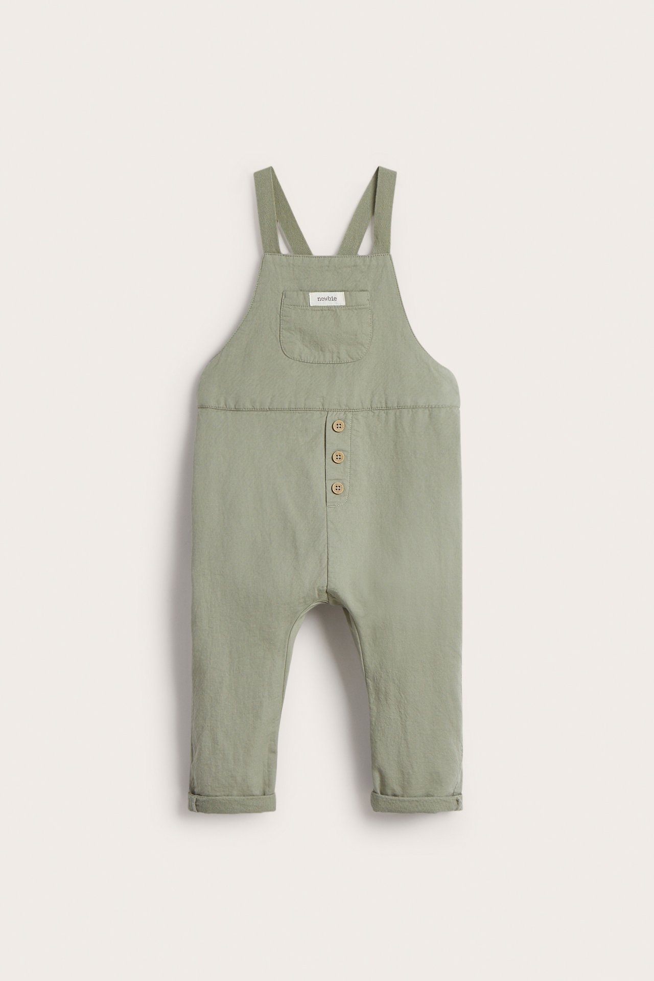 Vorderansicht: Baby-Latzhose aus grünem Baumwollgewebe mit Brusttasche, Knöpfen vorne und umgeschlagenen Bündchen.