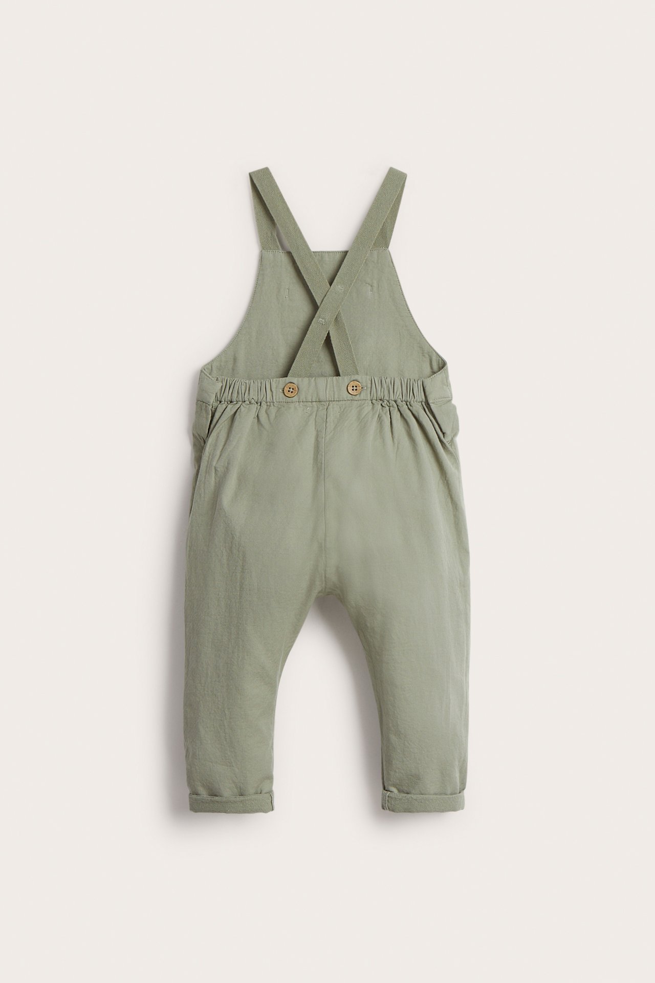 Rückenansicht von Baby-Latzhose aus grünem Baumwollgewebe mit verstellbaren Trägern und umgekrempelten Bündchen.