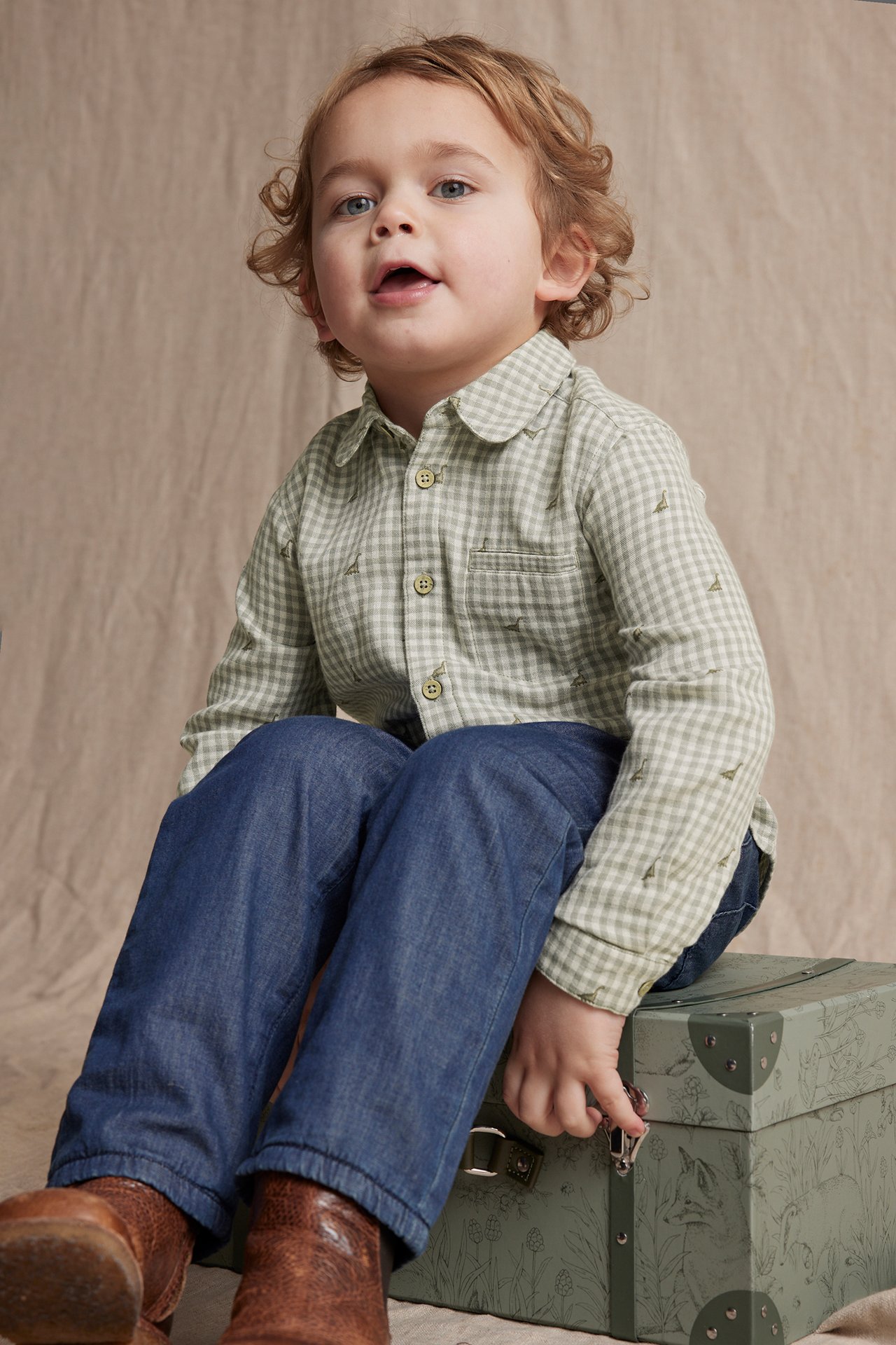 Front view of a kid in a light green checkered cotton shirt, blue trousers, and brown boots.
