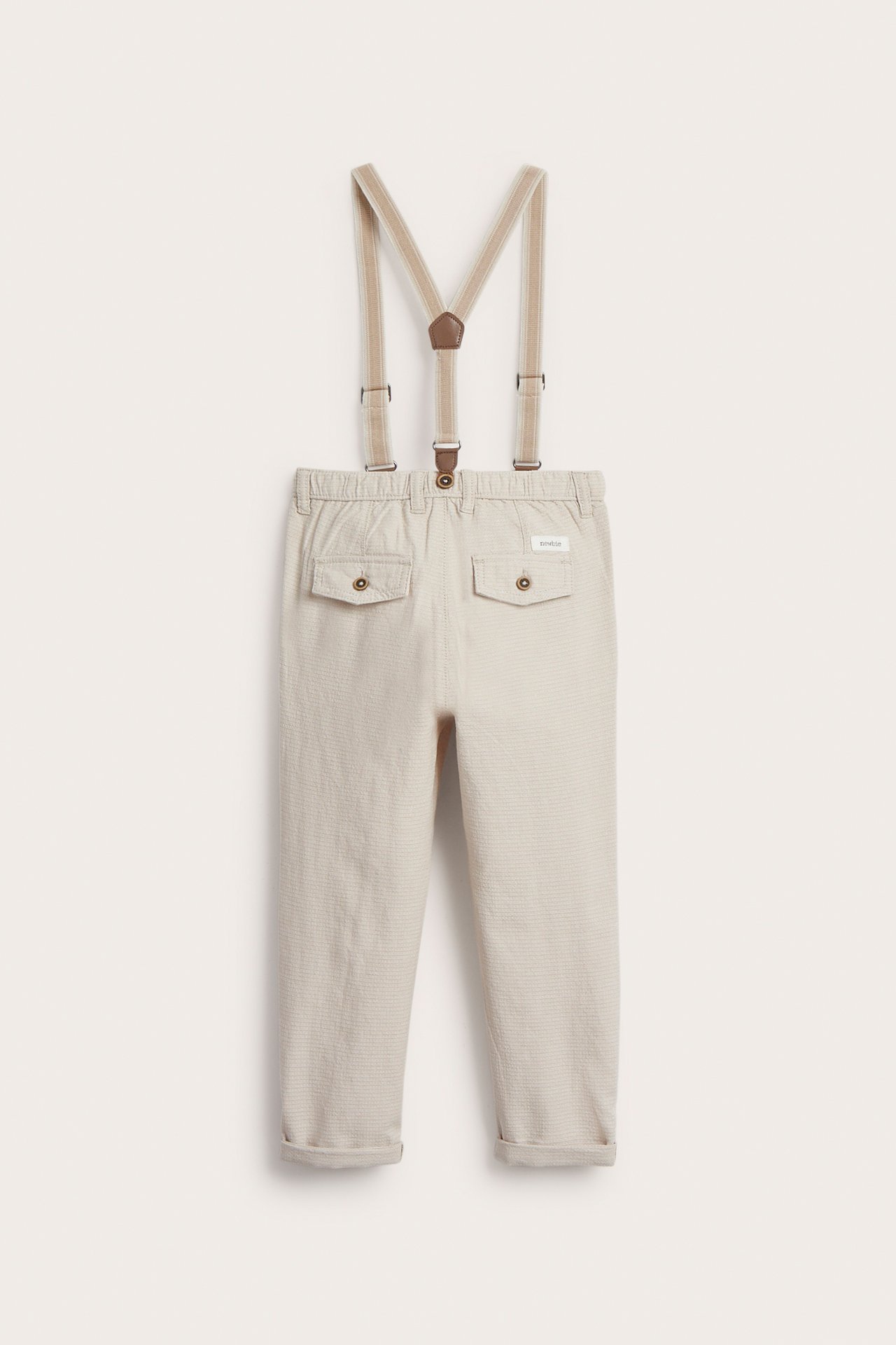 Front view of kid's beige woven dungarees with adjustable suspenders, decorative pockets, and rolled-up legs.