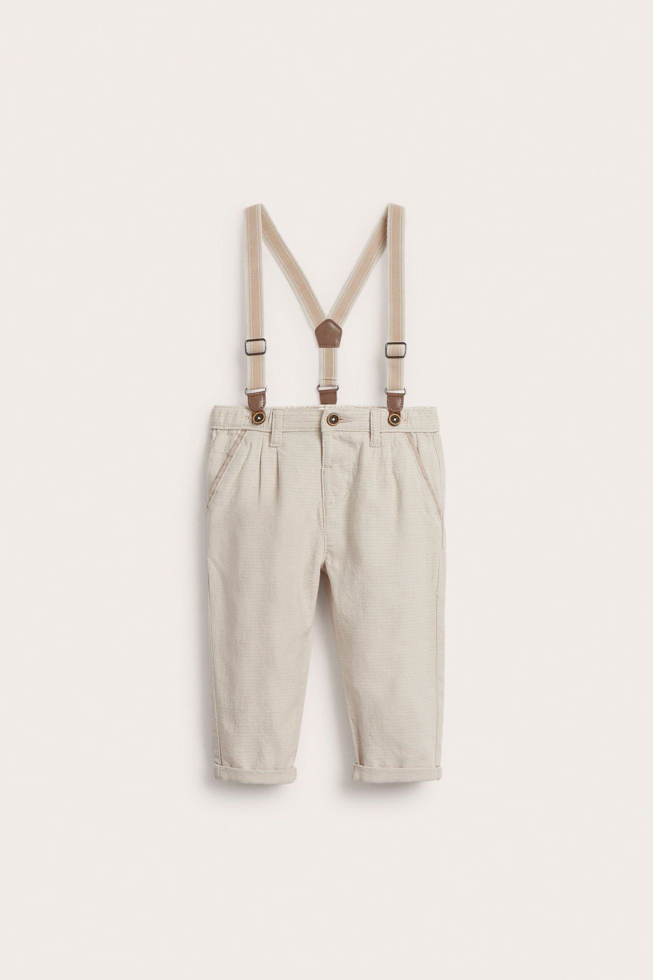 Vorderansicht beiger gewebter Kinderhosen mit verstellbaren Hosenträgern, umgekrempelten Beinen und Ziertaschen.