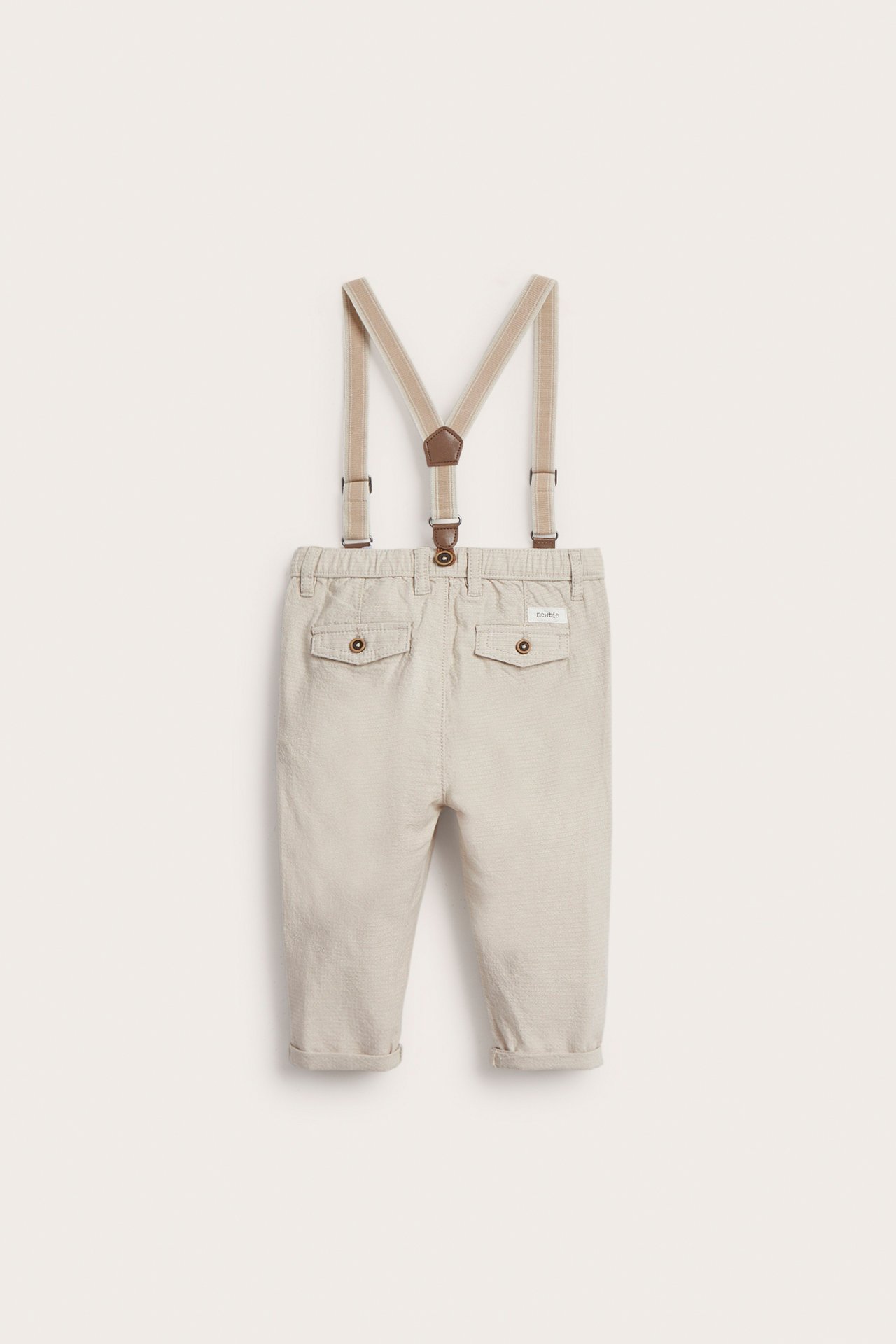 Vorderansicht beiger gewebter Baumwollhose mit verstellbaren Hosenträgern, Ziertaschen und hochgekrempelten Beinen.
