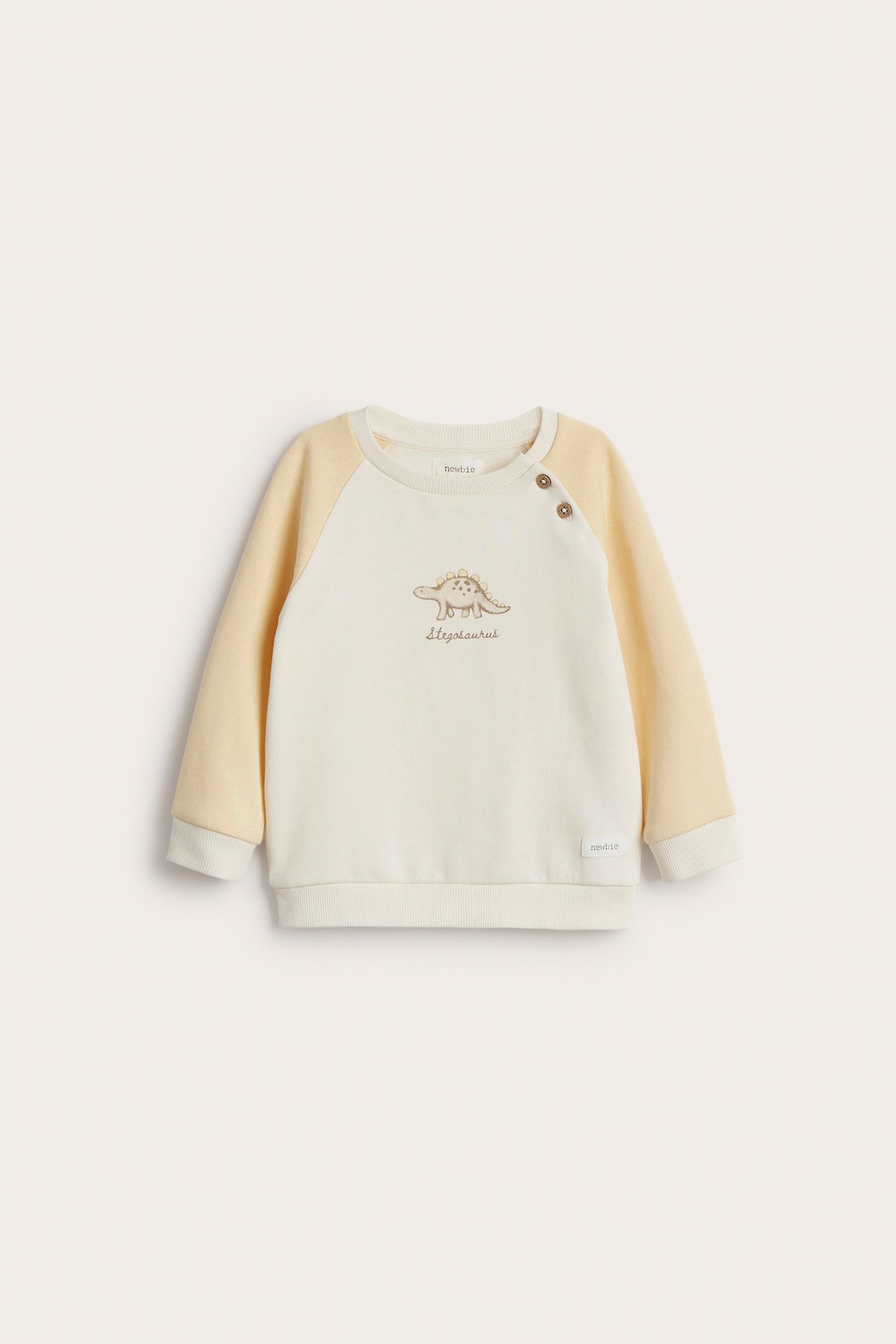 Front view of a kid's off-white and light yellow cotton sweatshirt with a dinosaur print and two buttons.
