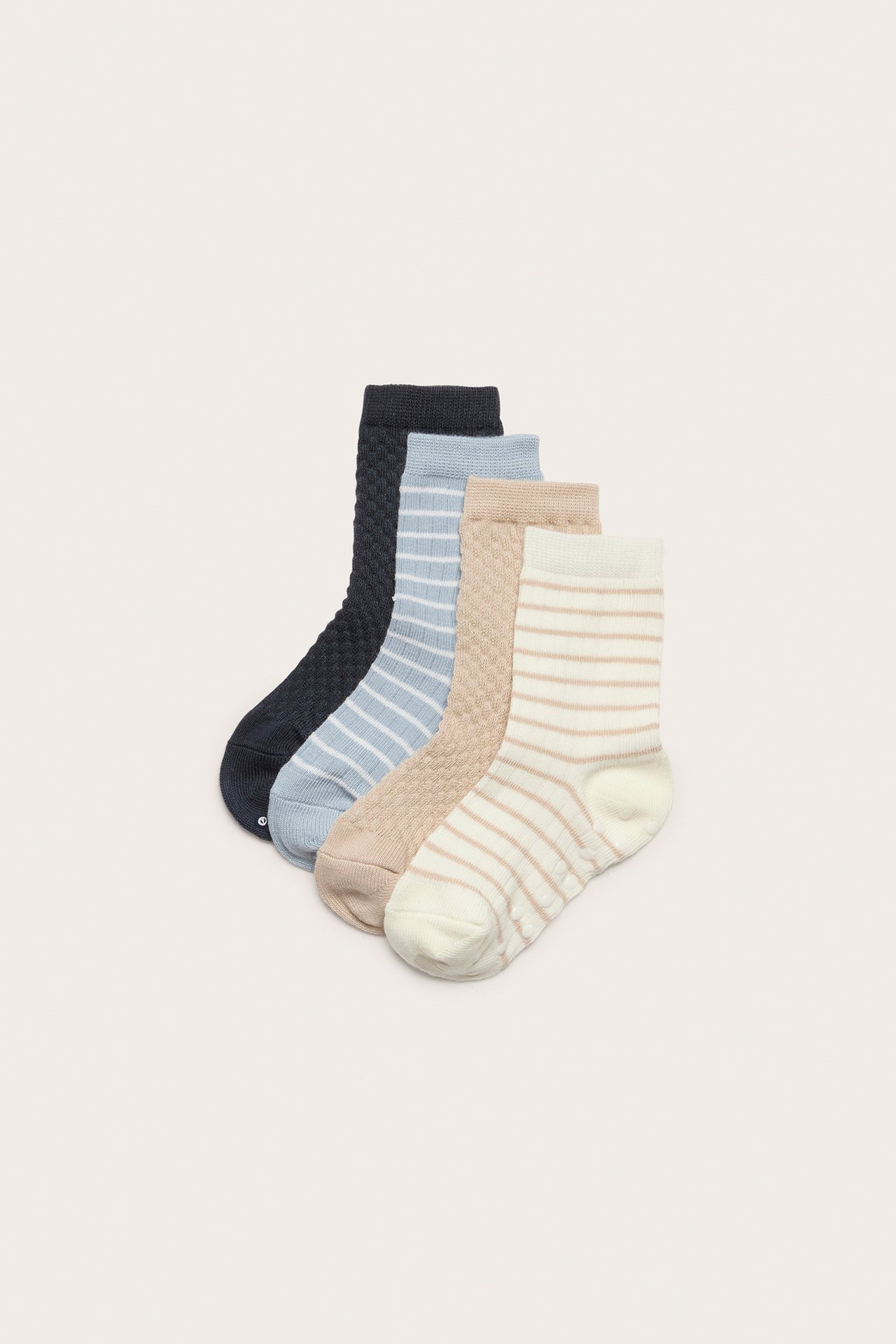 Draufsicht auf vier Kinder-Socken: cremeweiß gestreift, beige strukturiert, hellblau gestreift und dunkelblau strukturiert.