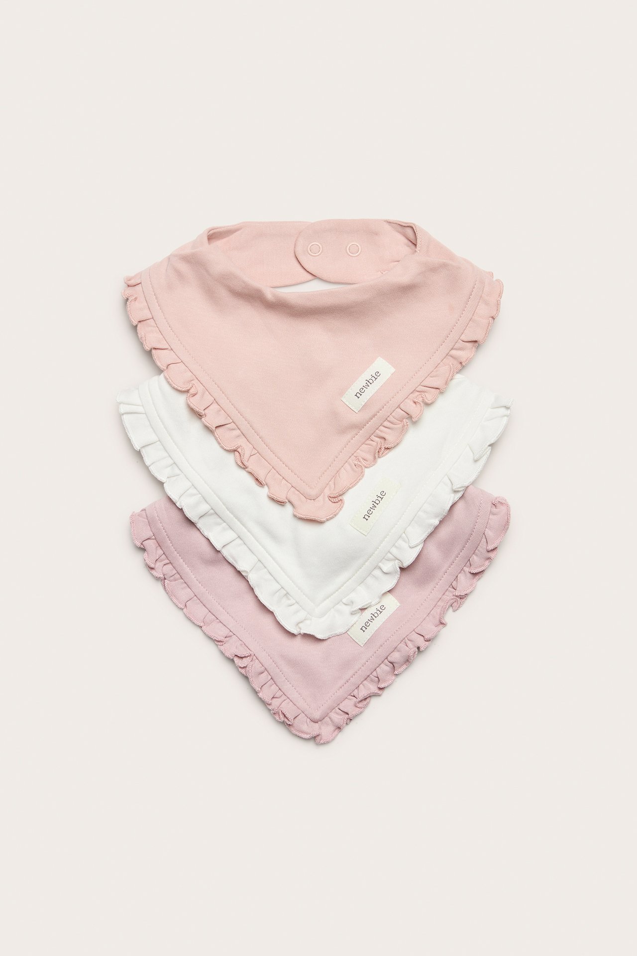 Three baby cotton bibs with ruffled edges and snap fastenings, in white, light pink, and dusty pink.