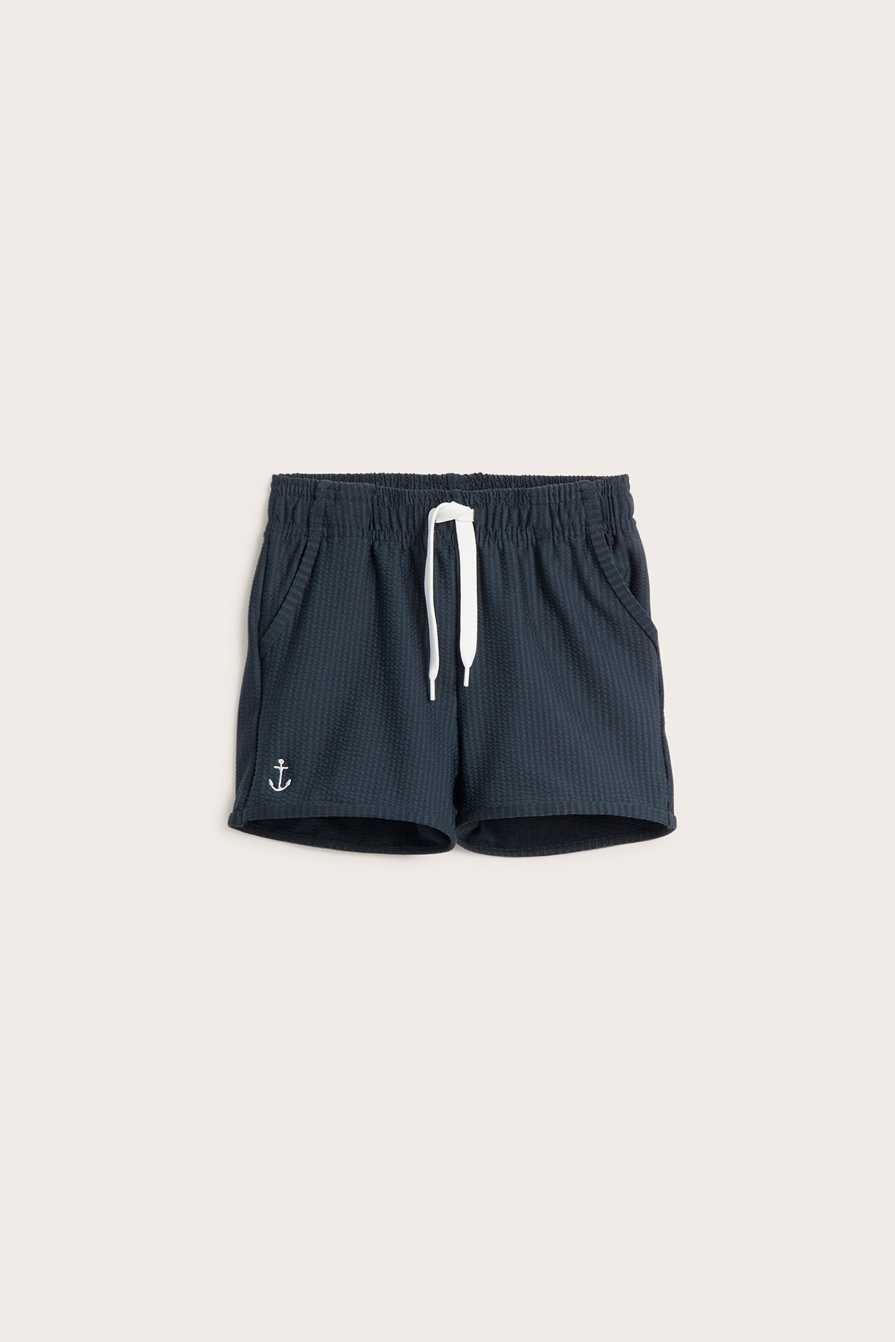 Vorderansicht dunkelblauer Kinder-Badeshorts aus Strukturjersey mit weißem Kordelzug und Ankerstickerei.