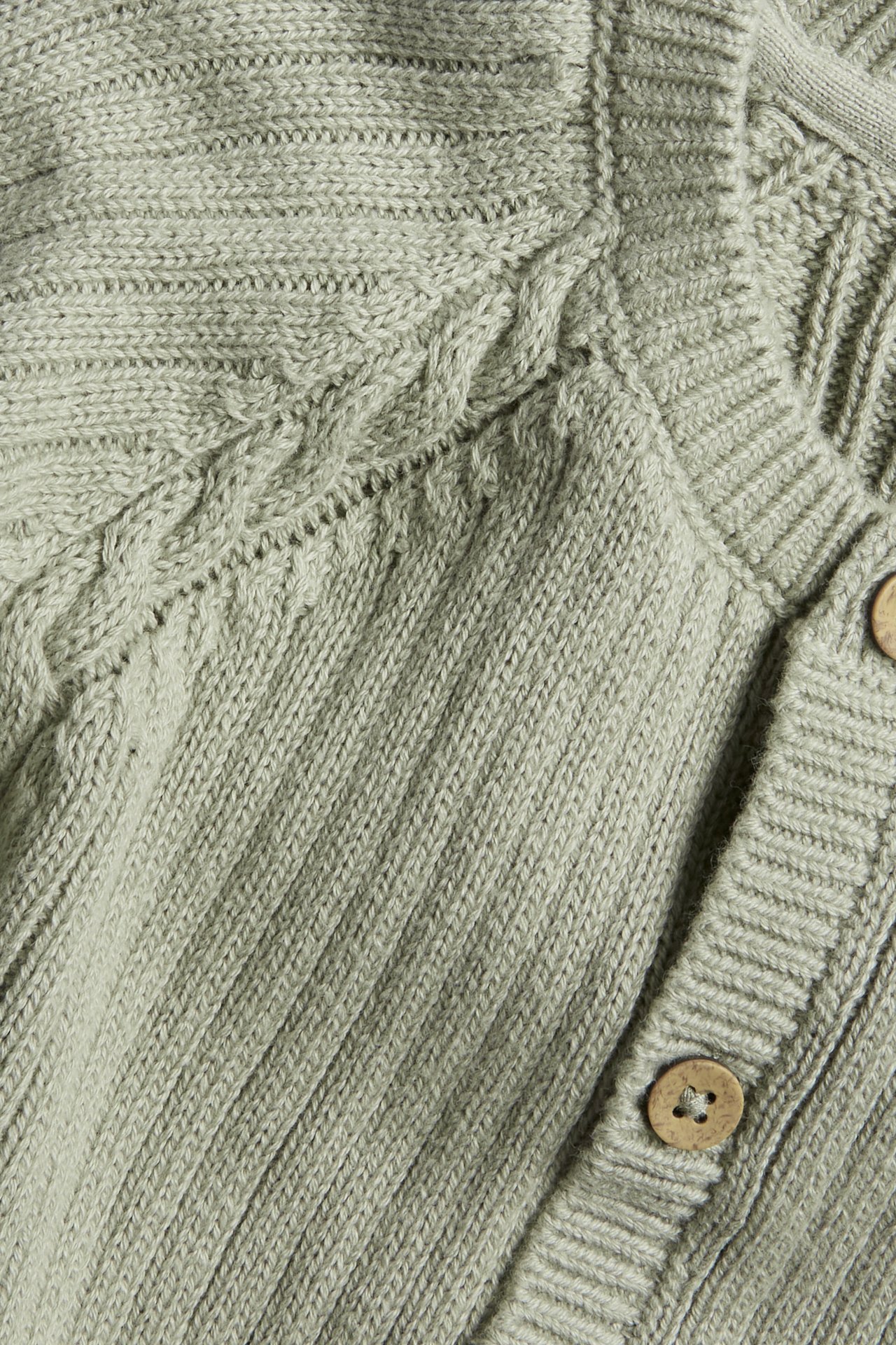 Nahaufnahme einer hellgrünen gestrickten Baumwollstrickjacke mit Zopfmusterärmeln und Holzknöpfen.