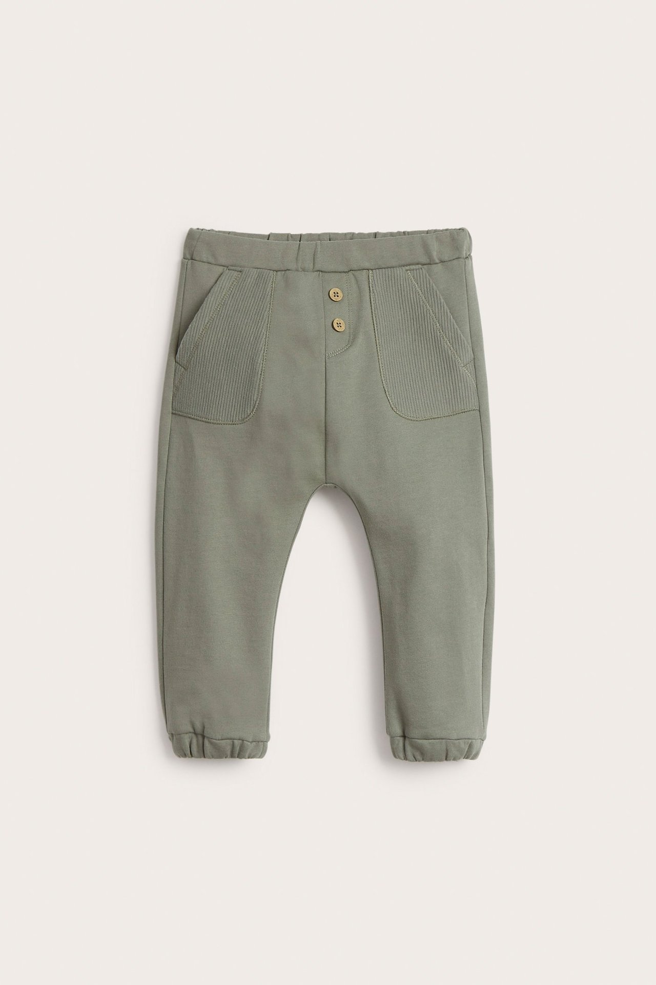 Front view of dark green cotton jogging pants with decorative buttons and ribbed patch pockets.