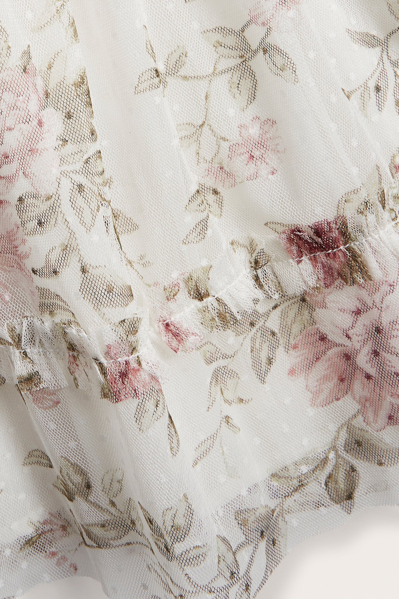 Close-up of an off-white mesh dress with pink floral pattern, dot structure, and ruffle detail.