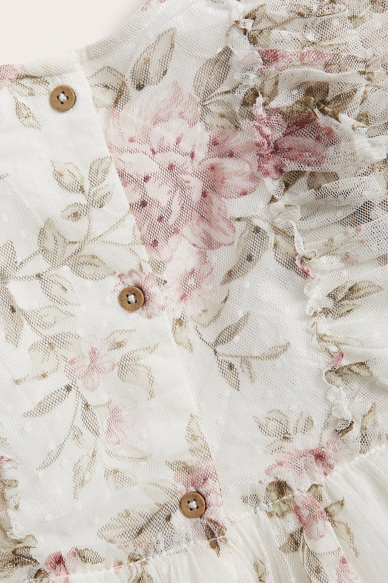 Close-up of an off-white mesh dress with pink floral print, dot texture, ruffles, and wooden buttons.