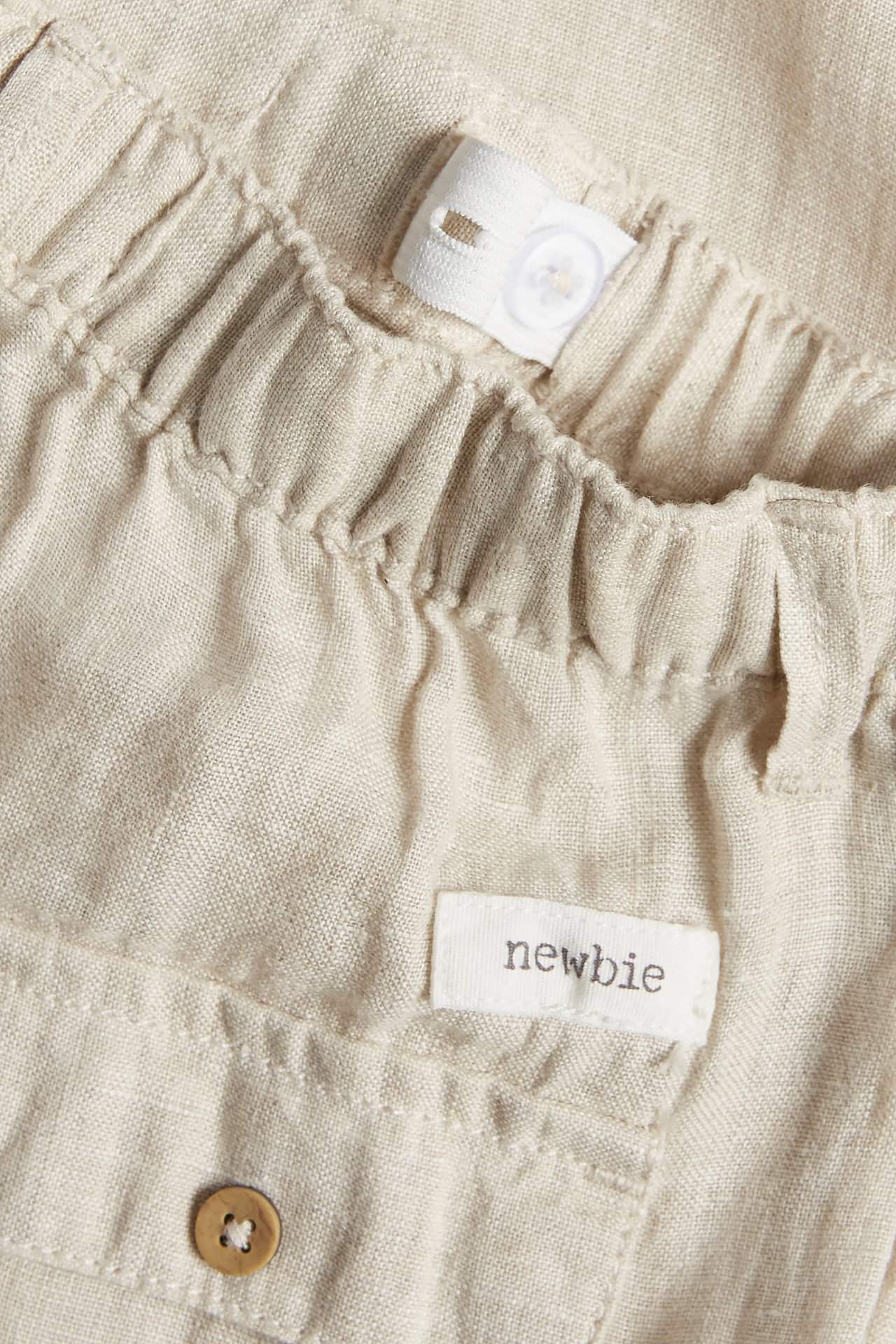 Nahaufnahme von hellbeiger Leinenhose mit Gummizugbund, verstellbarem Innenband und Zierknopf.