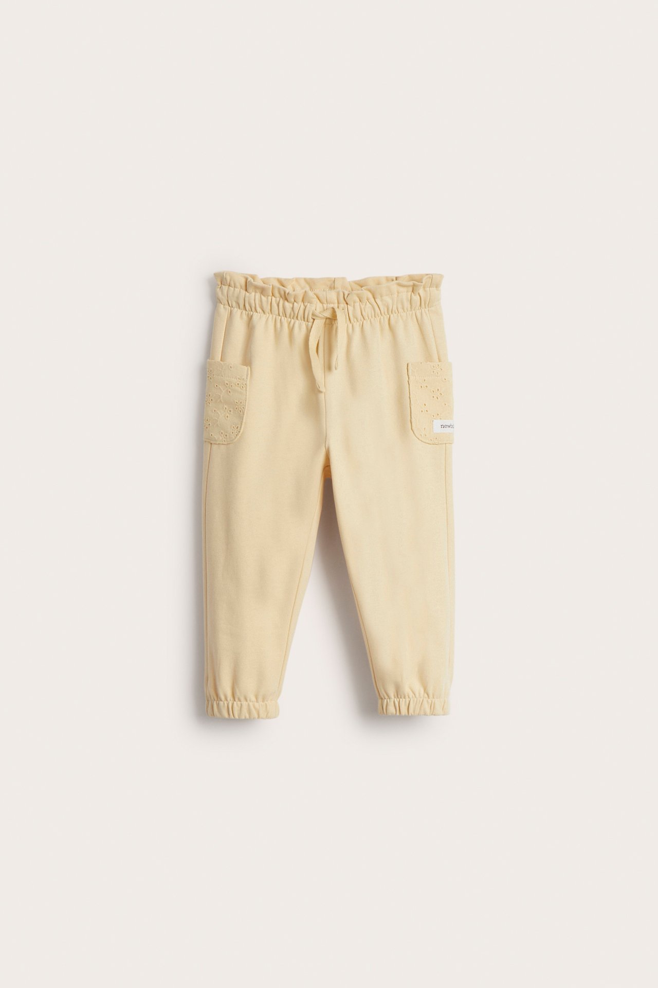 Vorderansicht: gelbe Kinder-Jogginghose aus Baumwolle mit Rüschenbund, Kordelzug und bestickten Taschen.