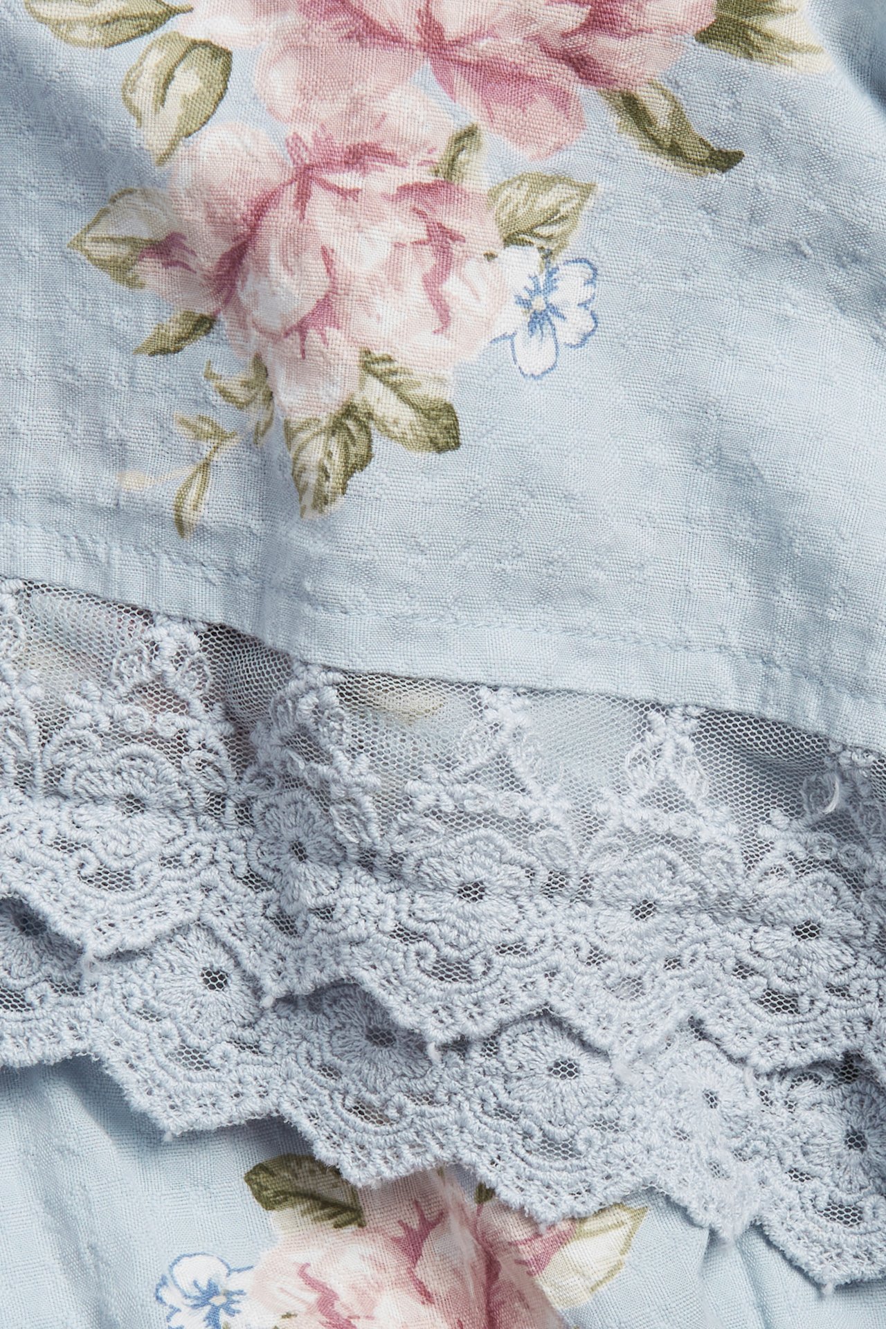 Nahaufnahme eines hellblauen geblümten Baumwollkleides mit rosa Blumen und passender blauer Spitzenborte.