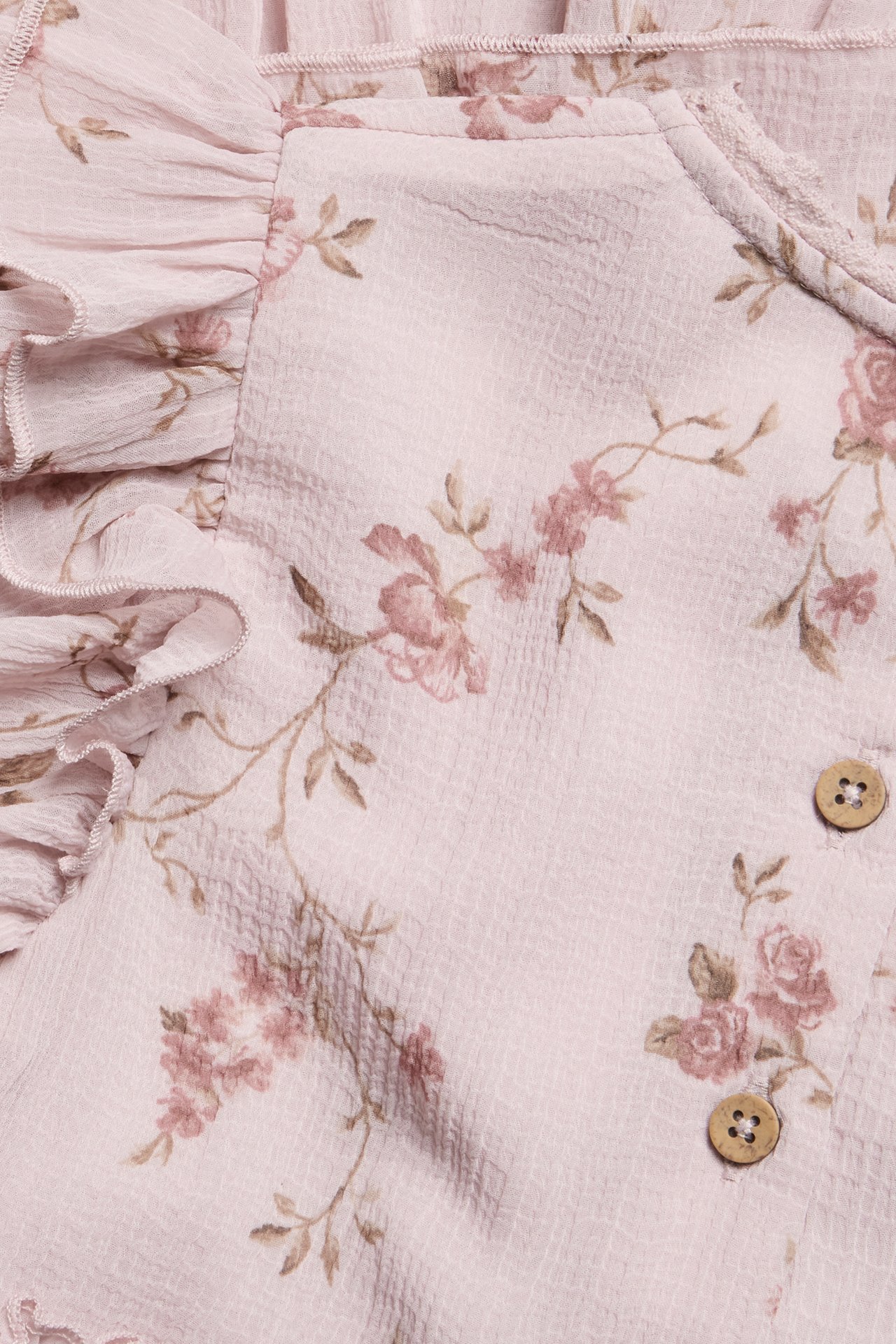Nahaufnahme eines rosa geblümten Chiffonkleides mit Rüschen und Holzknöpfen.