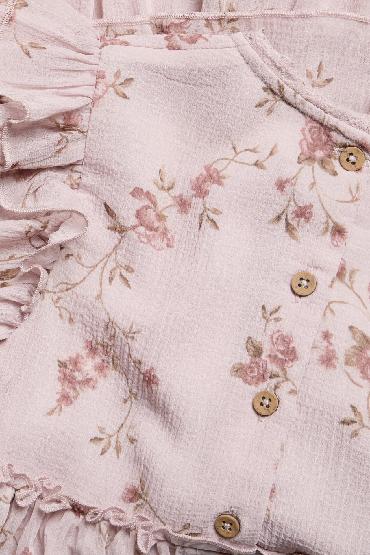 Close-up of a pink floral chiffon dress with ruffles, textured fabric, and small wooden buttons.